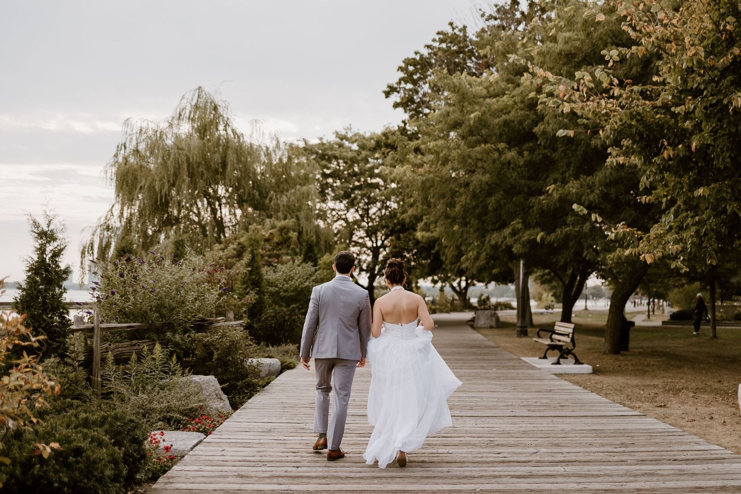 Newlyweds walking hand in hand on a wooden boardwalk surrounded by trees.