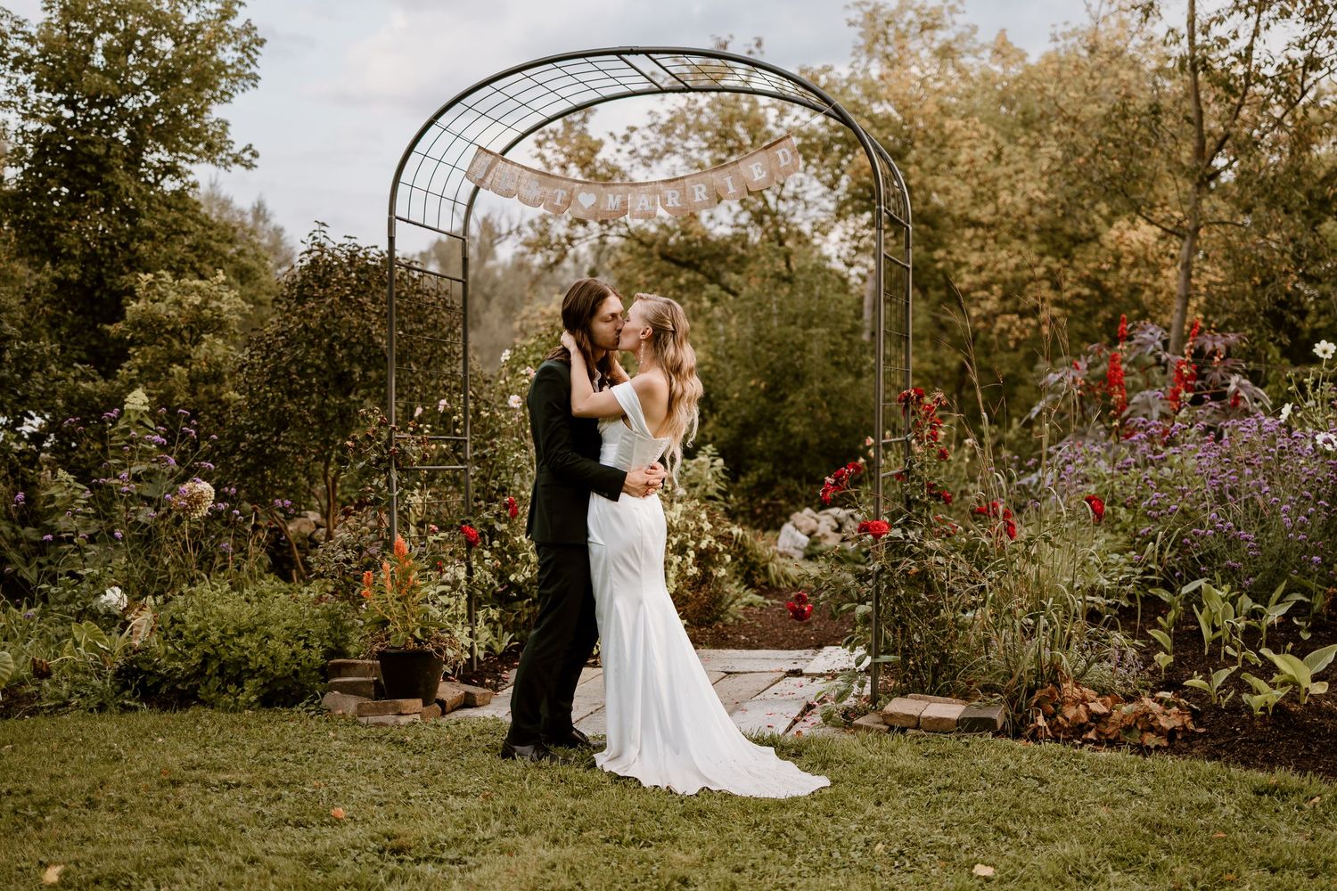 Intimate wedding ceremony under a metal garden arch surrounded by colorful flowers.