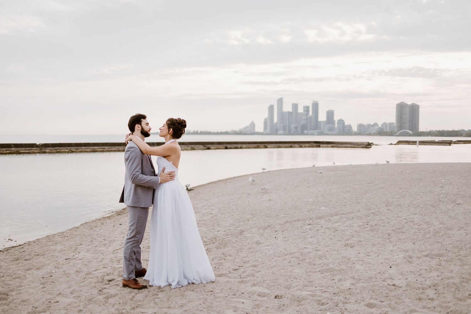 A romantic wedding portrait on a beach with a distant city skyline.