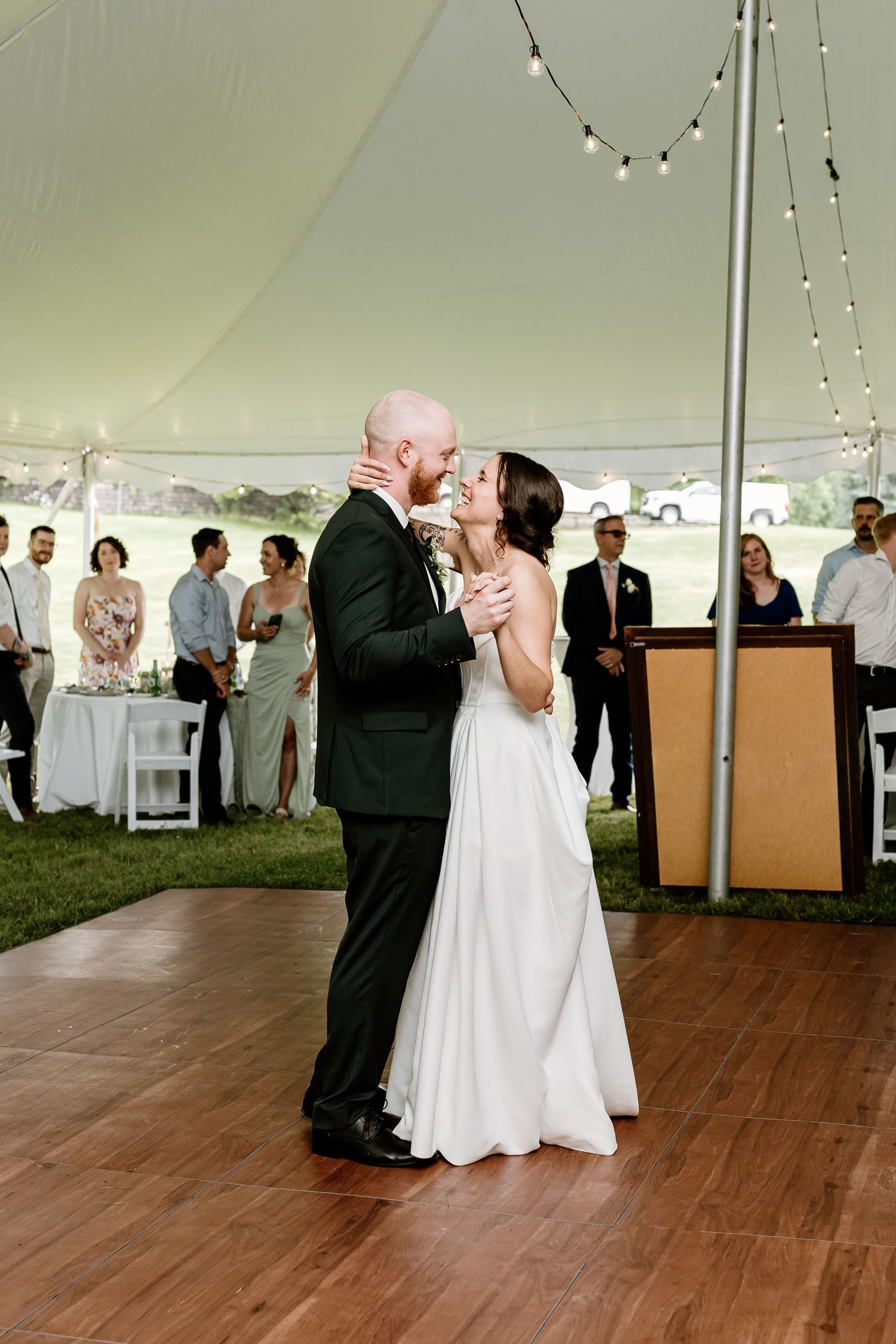 Romantic first dance under tent with string lights and guests watching.