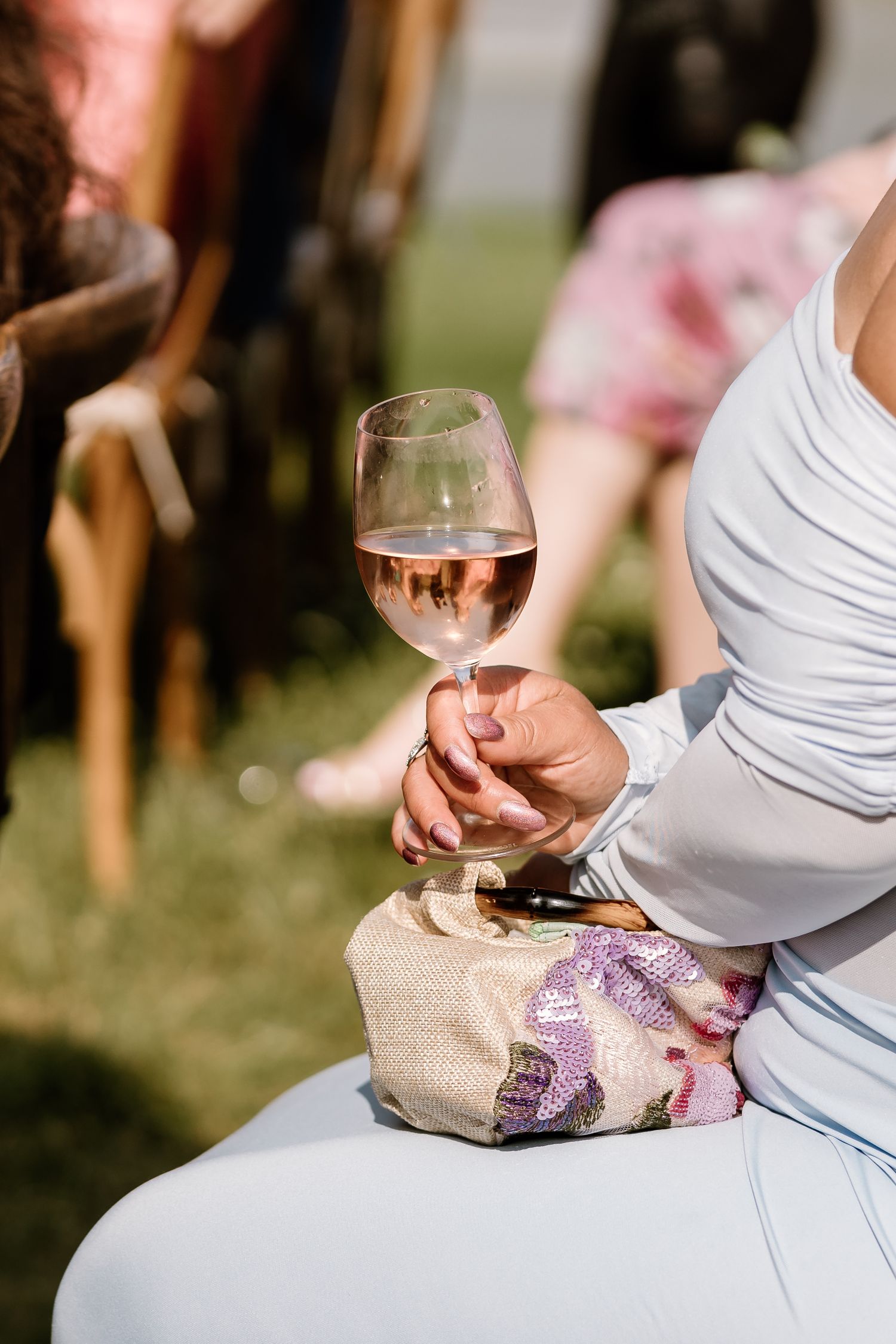 Close-up of rosé wine glass being held during outdoor wedding reception.