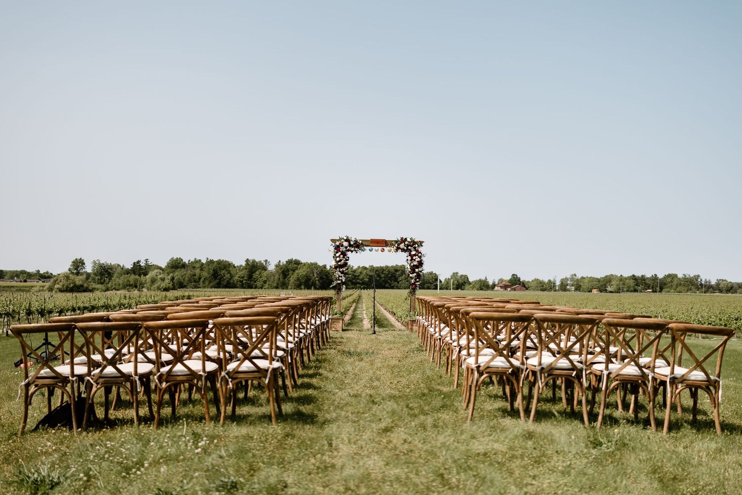 Rustic wooden chairs arranged in rows on a grassy field for an outdoor wedding ceremony.