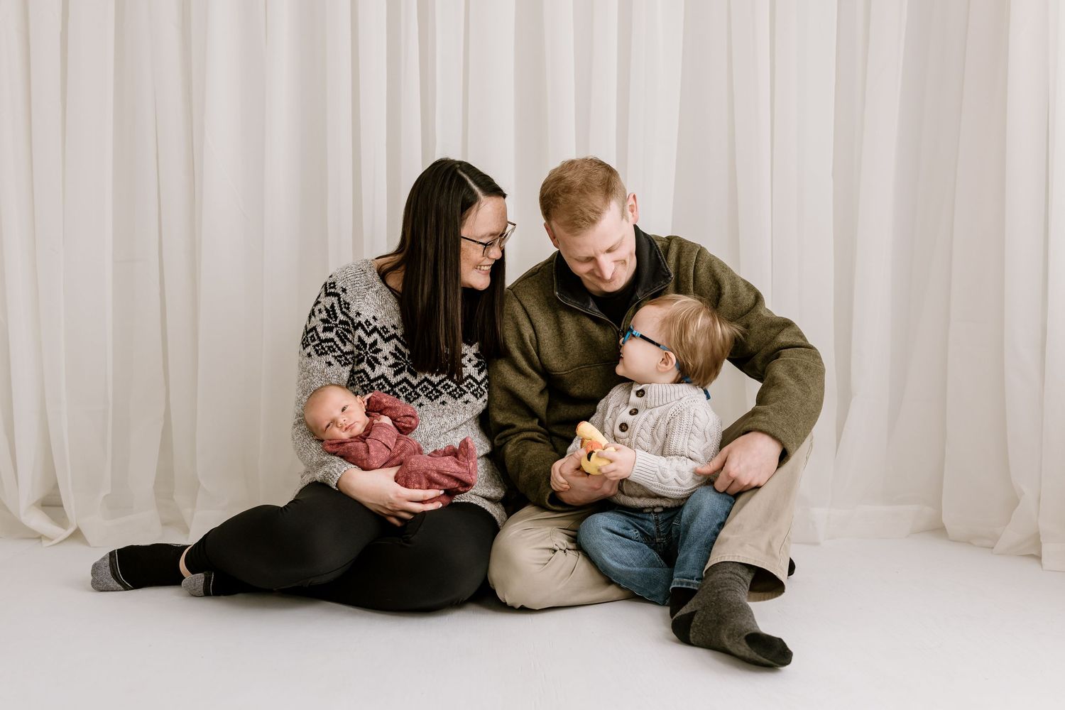 Casual family photo session with everyone sitting on floor against white backdrop.