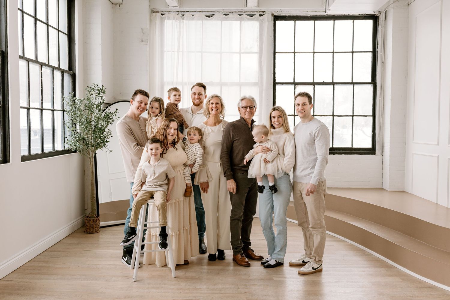Large family group portrait smiling together in bright modern studio with hardwood floors and large windows.