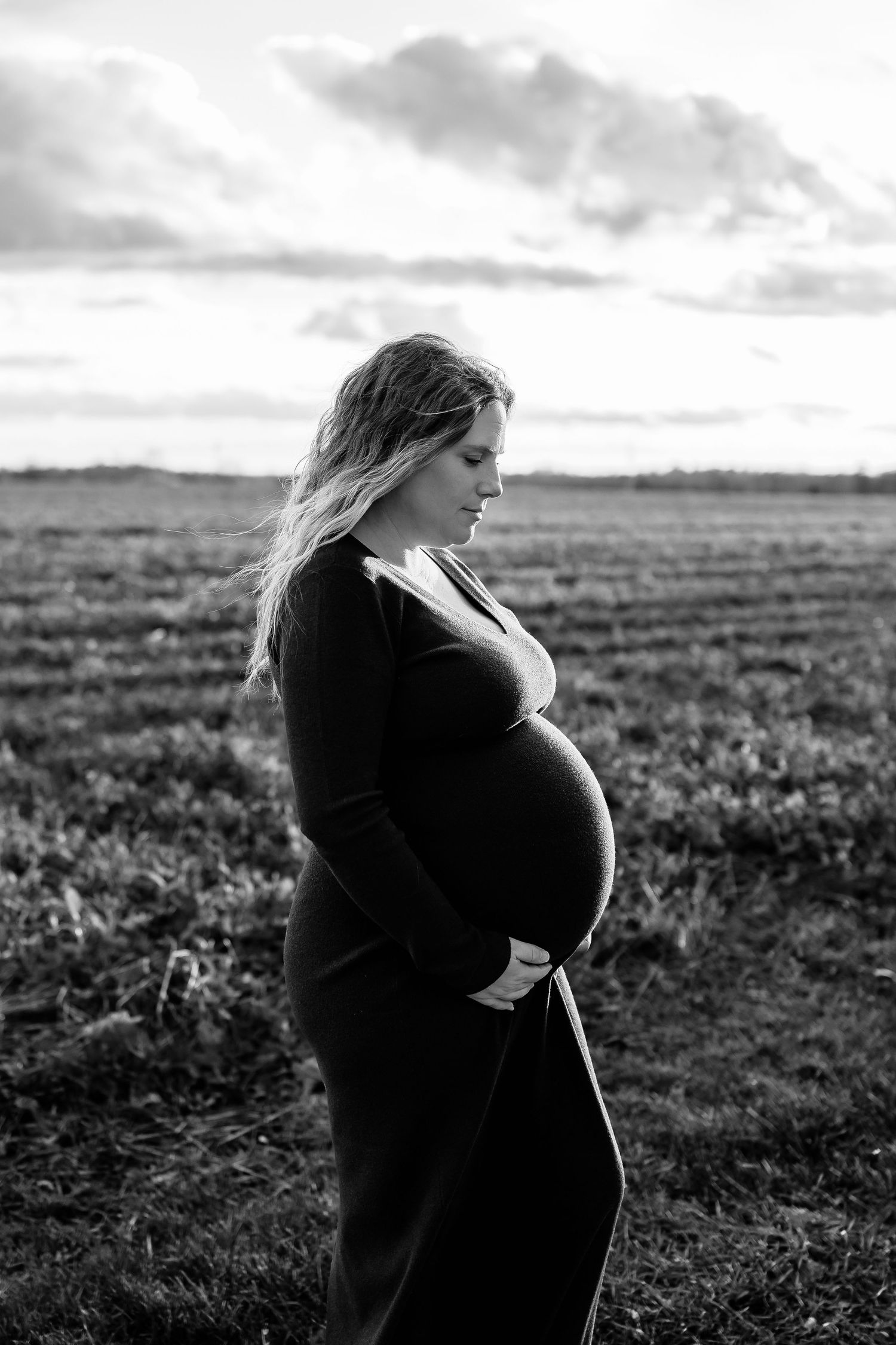 Black and white maternity photos taken in a field at sunset.