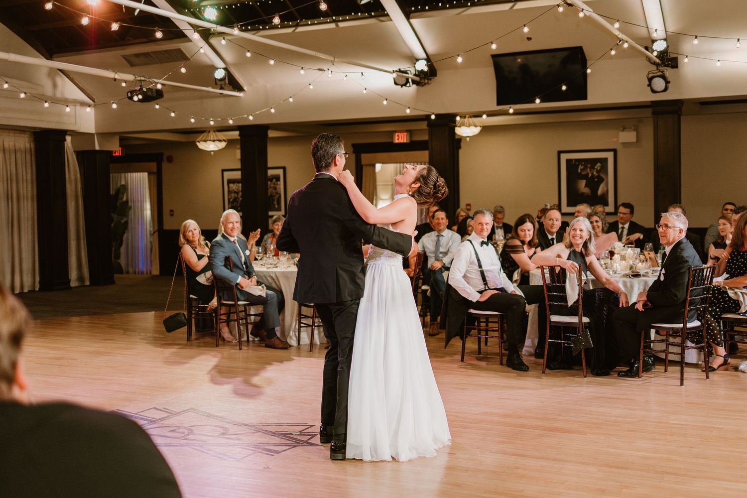 Wedding celebration in progress with guests watching dancers on the illuminated dance floor.