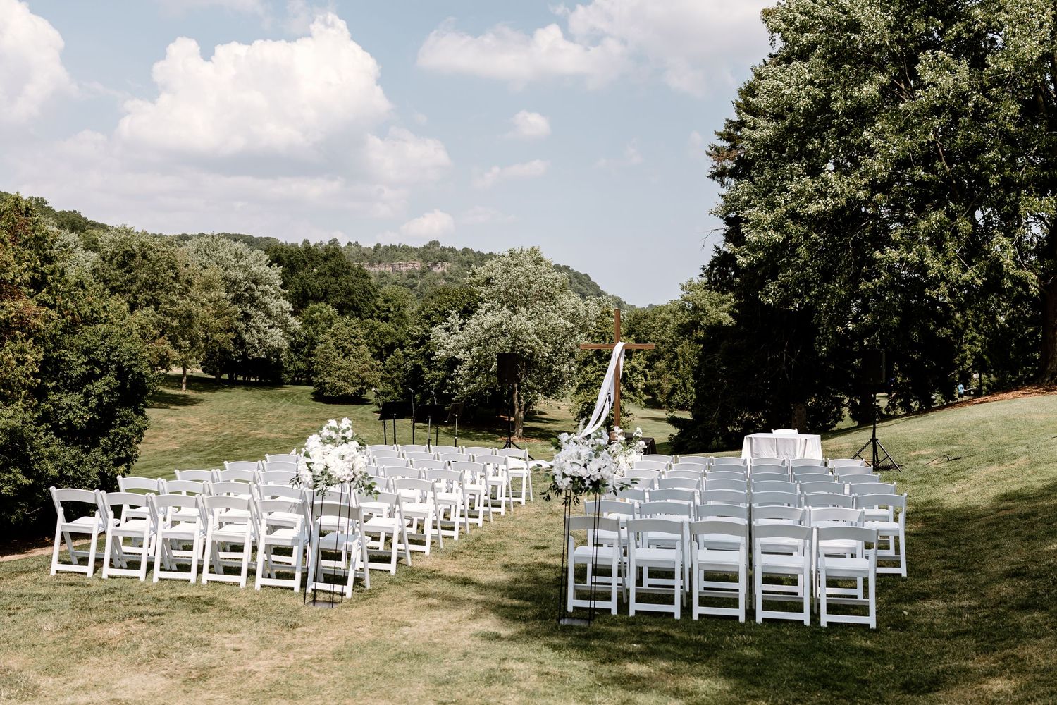 White chairs arranged for an outdoor wedding ceremony on a grassy hillside.