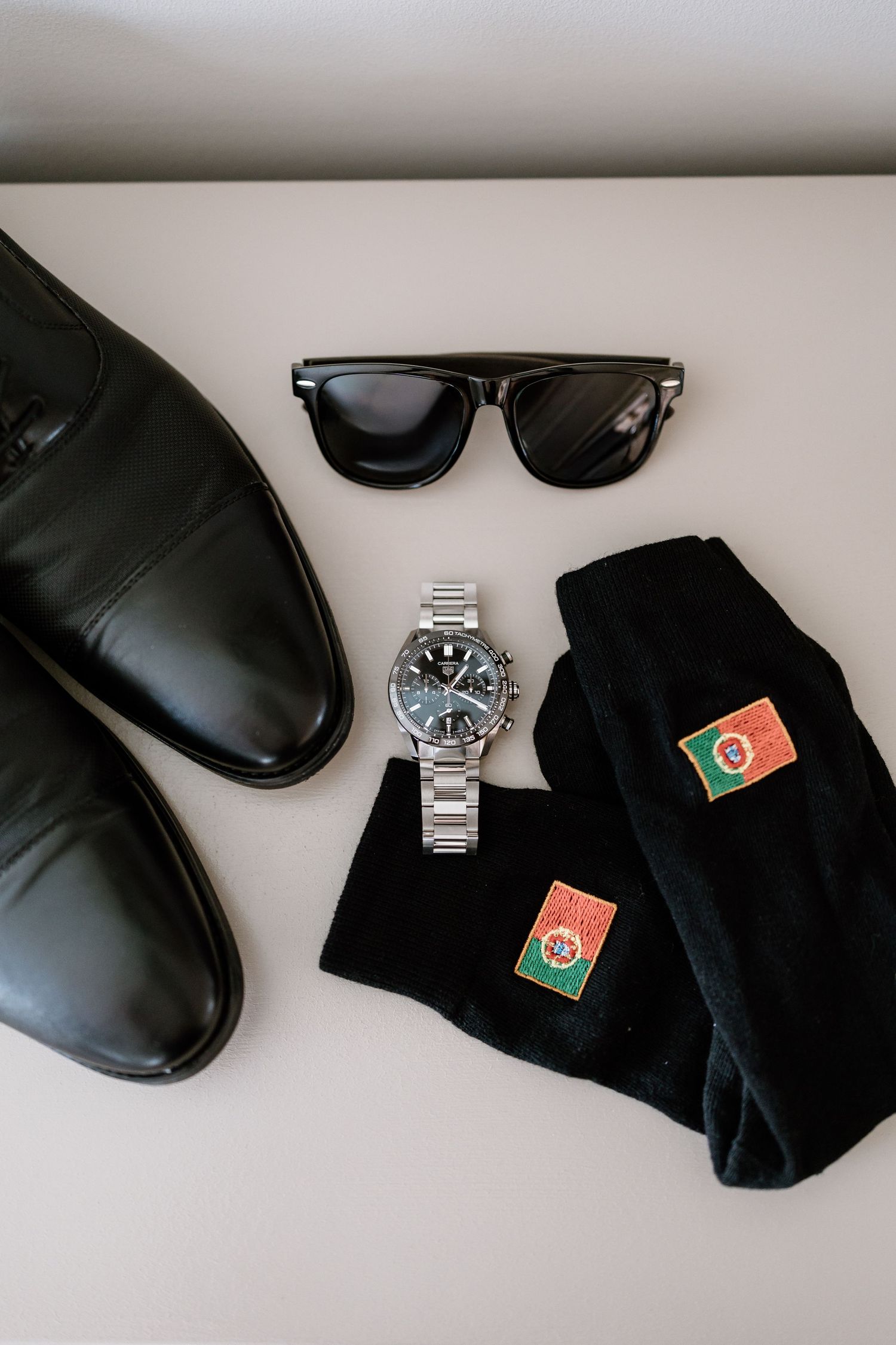 Men's formal accessories including black dress shoes, sunglasses, watch and socks on white background.