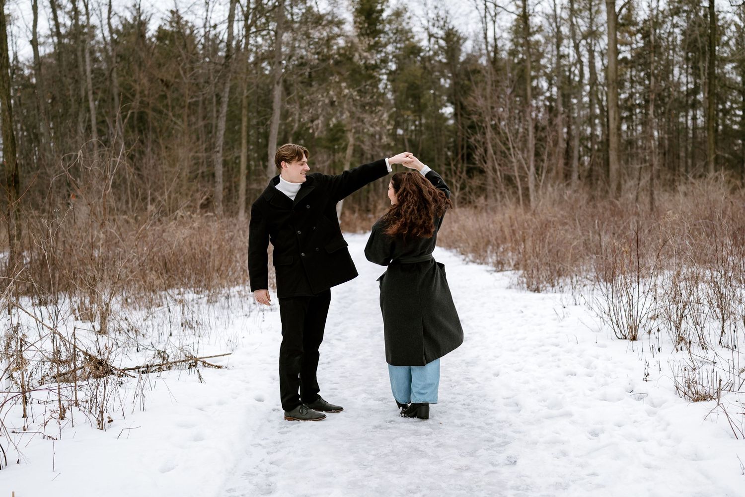 Couple sharing a dance move on snowy trail surrounded by winter forest.