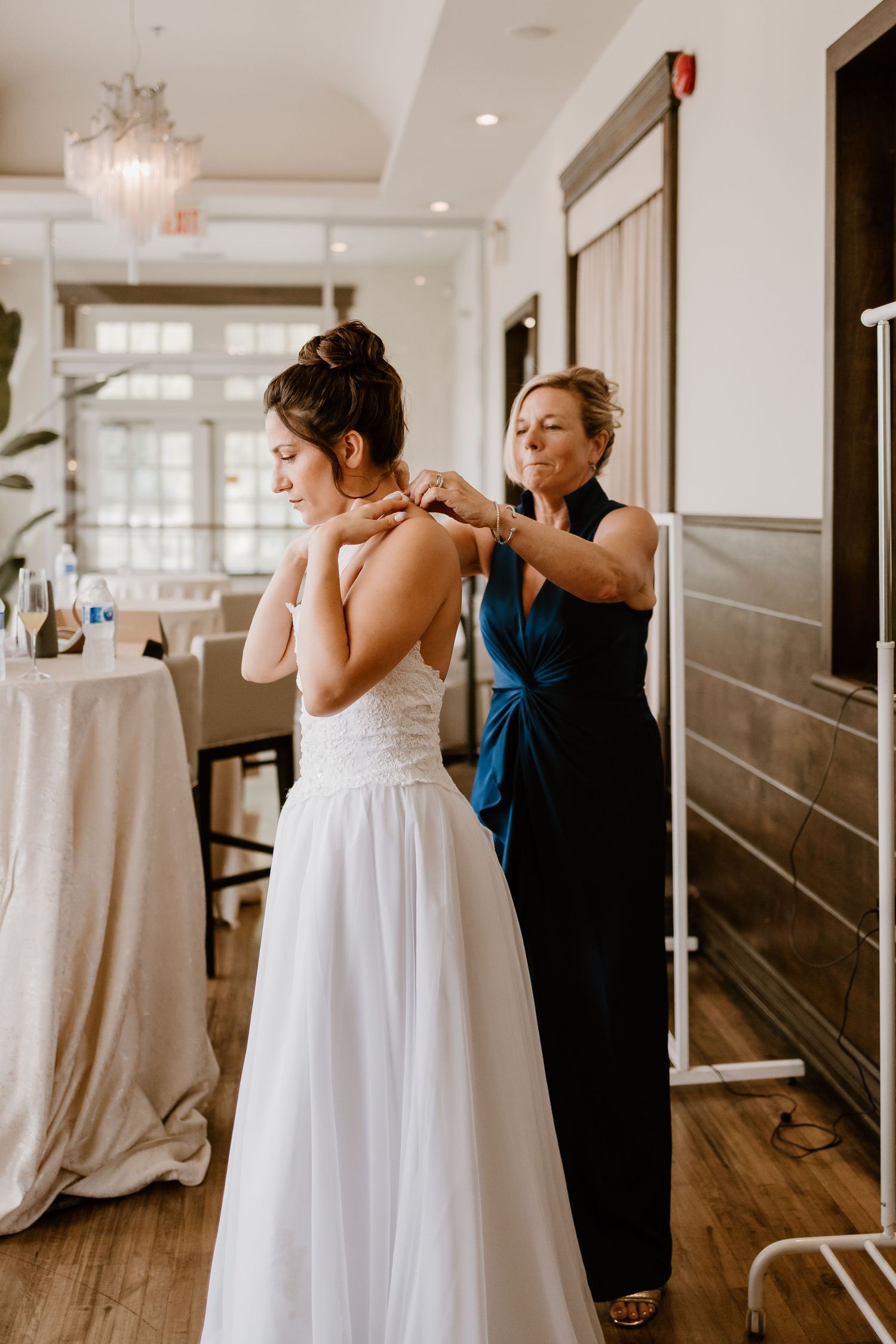 Final adjustments being made to white wedding gown in elegant venue setting.