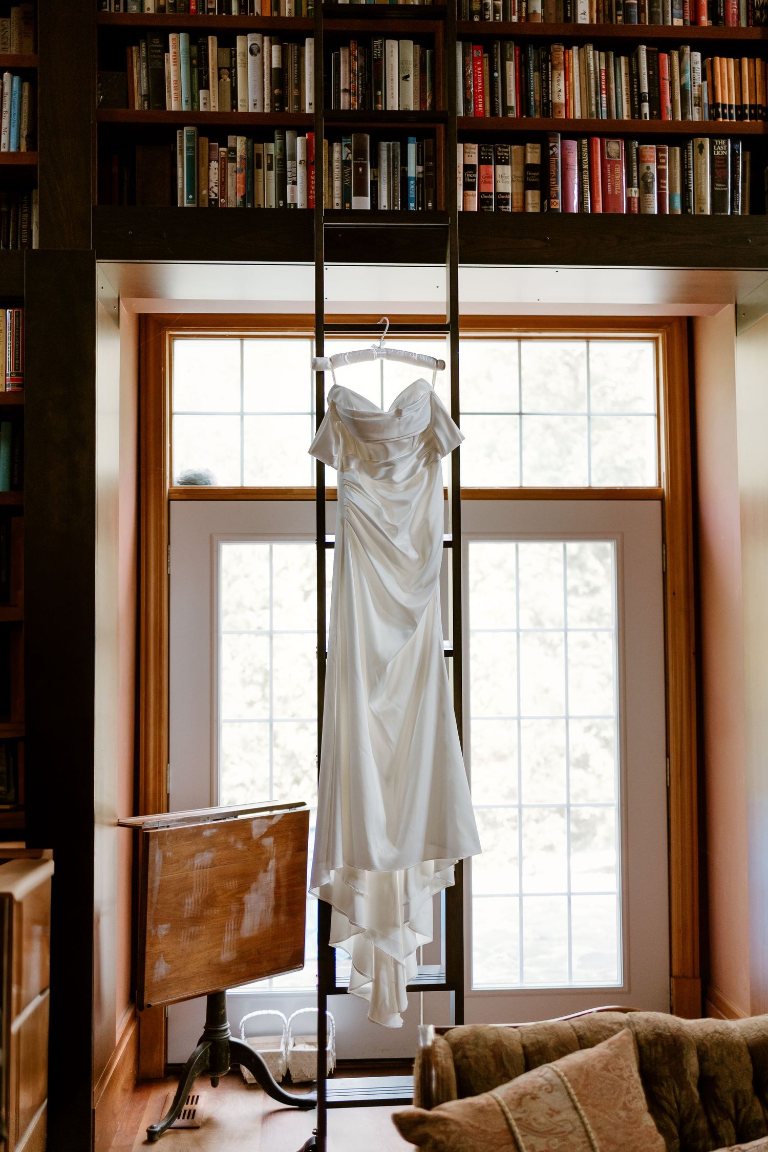 White wedding dress hanging in front of a bright window with natural light streaming in.