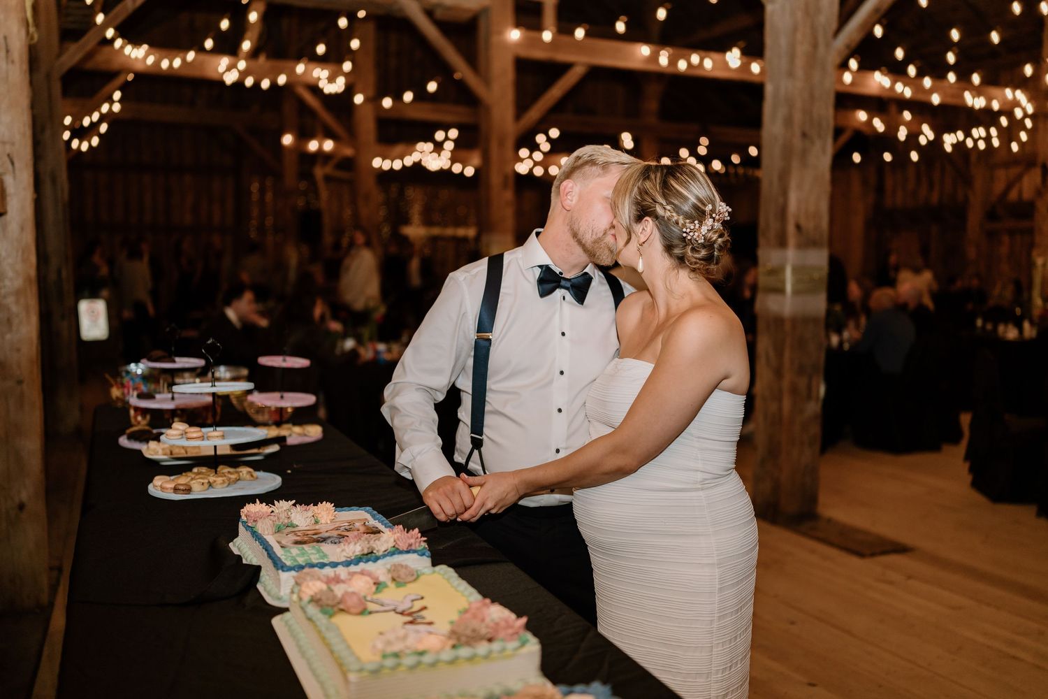 Wedding reception celebration inside rustic barn with twinkling lights and wooden beams.