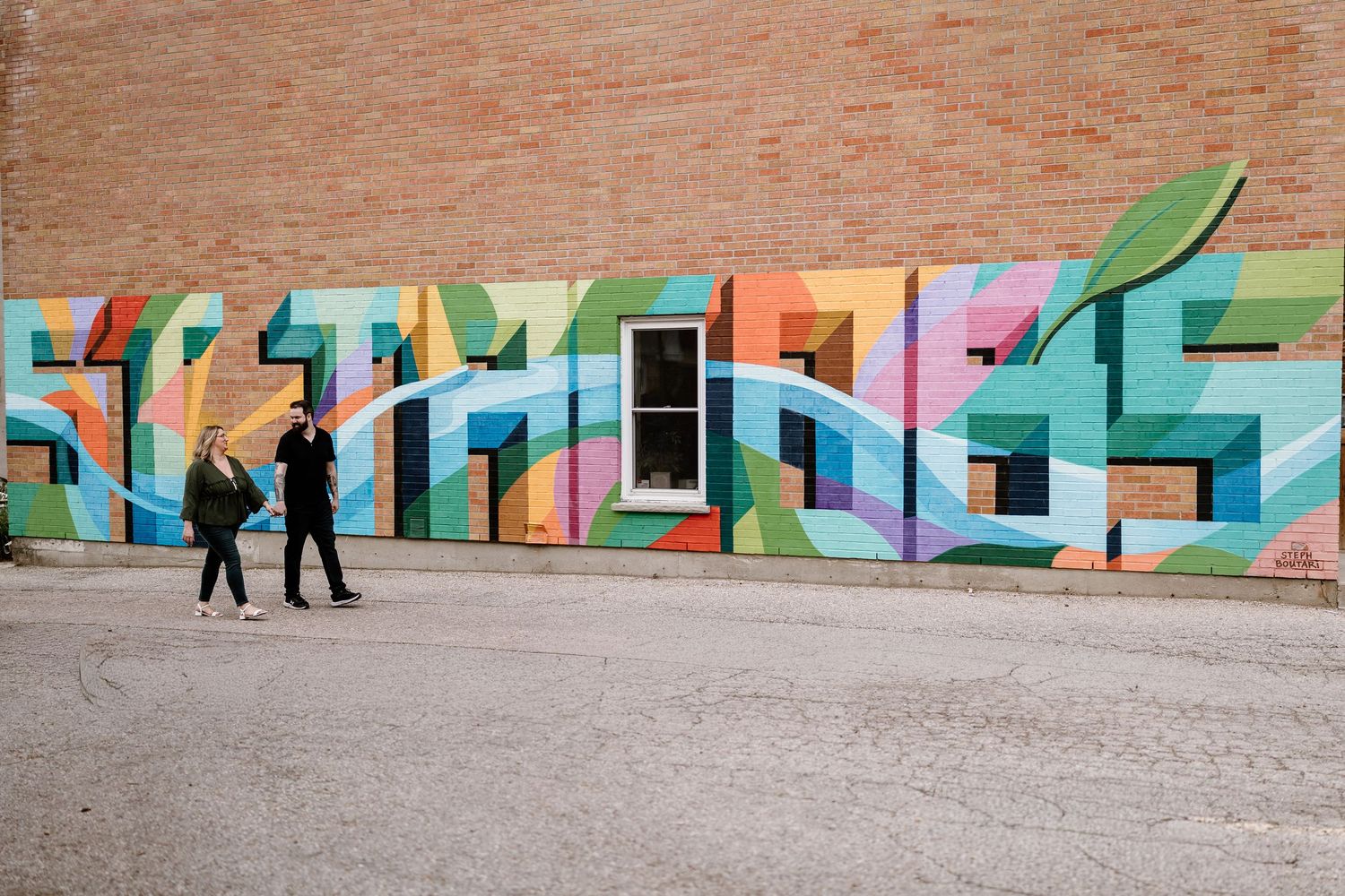 Colorful graffiti mural on brick wall with two people walking past in urban setting.