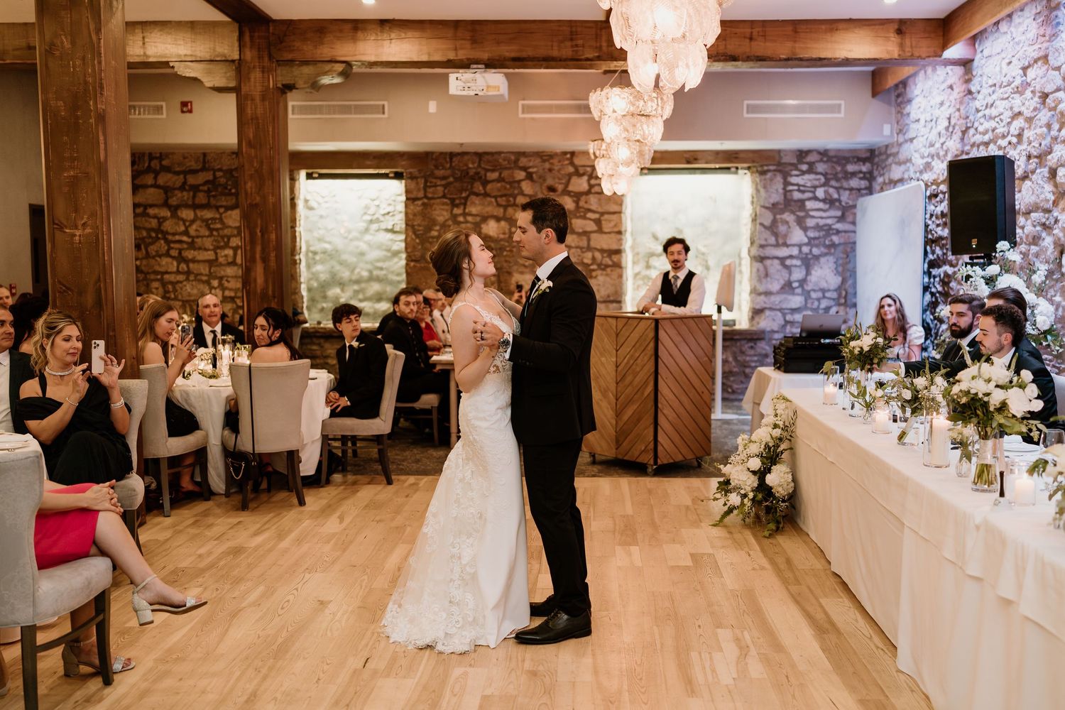 First dance in a rustic reception venue with stone walls and elegant chandeliers.