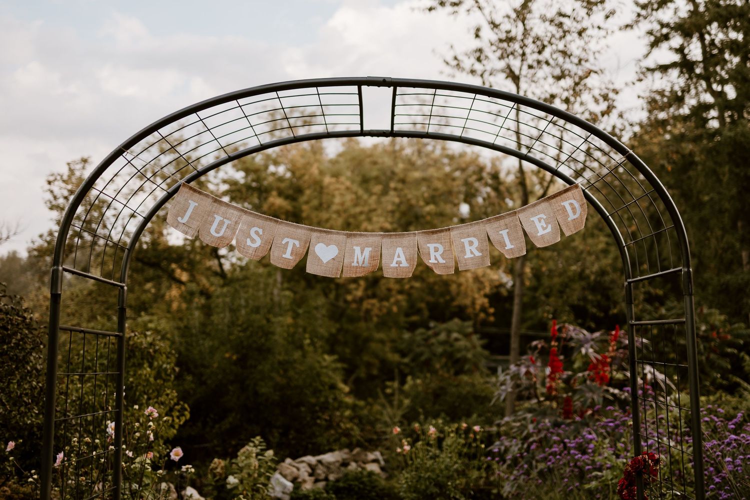 Garden arch decorated with a rustic banner for a wedding celebration in an autumn outdoor setting.