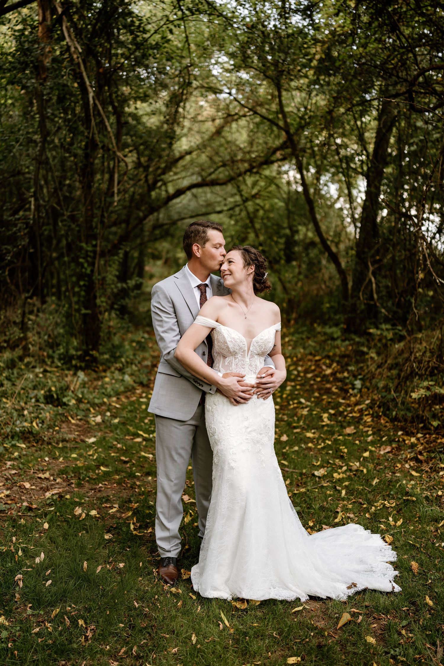 A tender moment between newlyweds surrounded by fall foliage in a wooded setting.