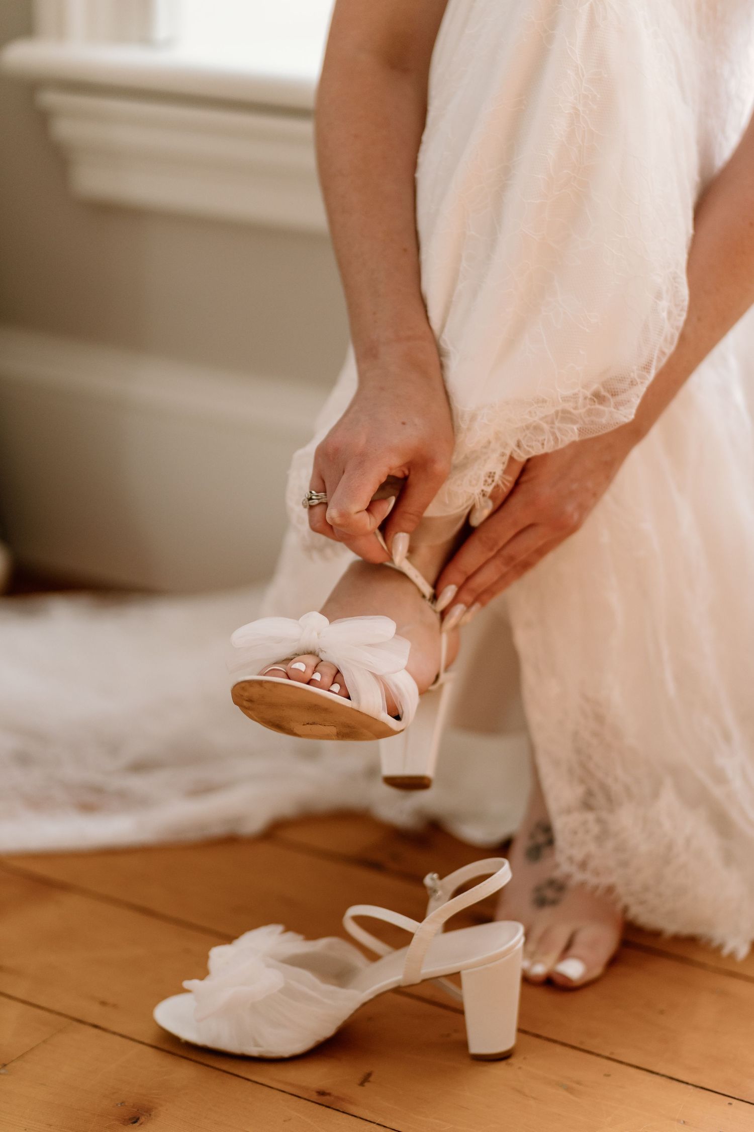 Hands fastening white wedding shoes on wooden floor.