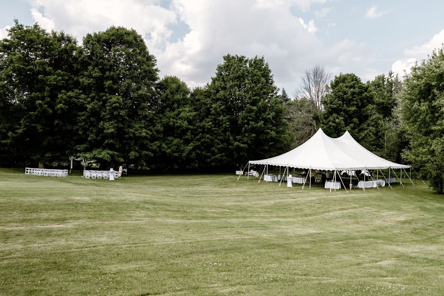 Panoramic view of white wedding tents set up on a spacious green lawn.