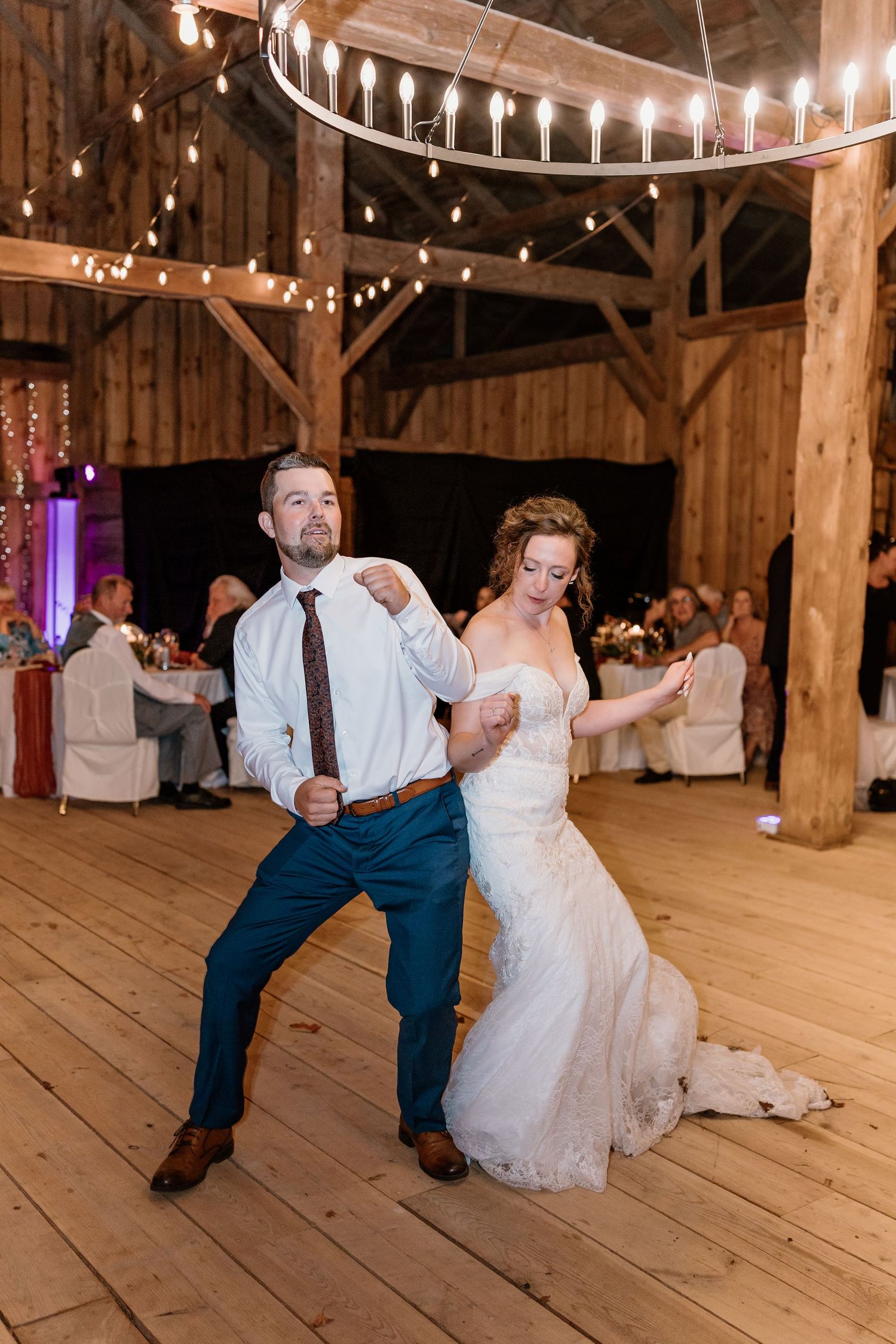 Wedding guests performing choreographed dance moves on a rustic wooden barn floor.