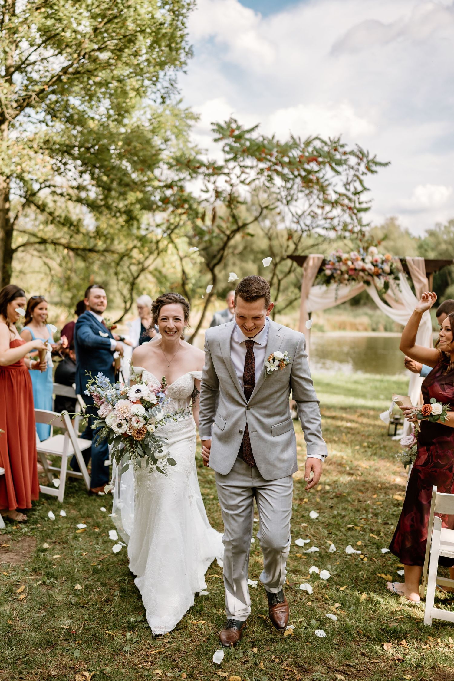 Newlyweds walk down the aisle while wedding guests celebrate with confetti in an outdoor ceremony.