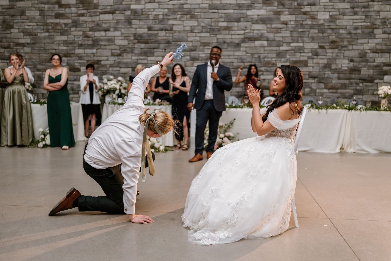 Bride and groom share a playful moment on the dance floor at their elegant wedding reception with guests watching.