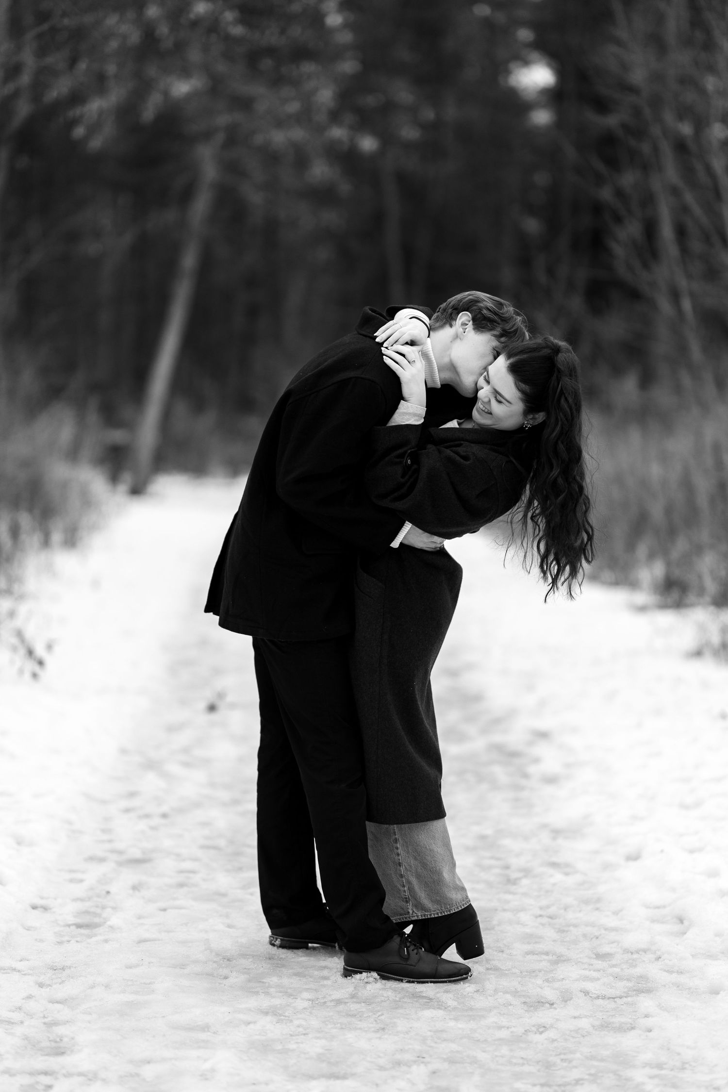 A black and white winter scene captures an intimate moment between a couple in the snow.