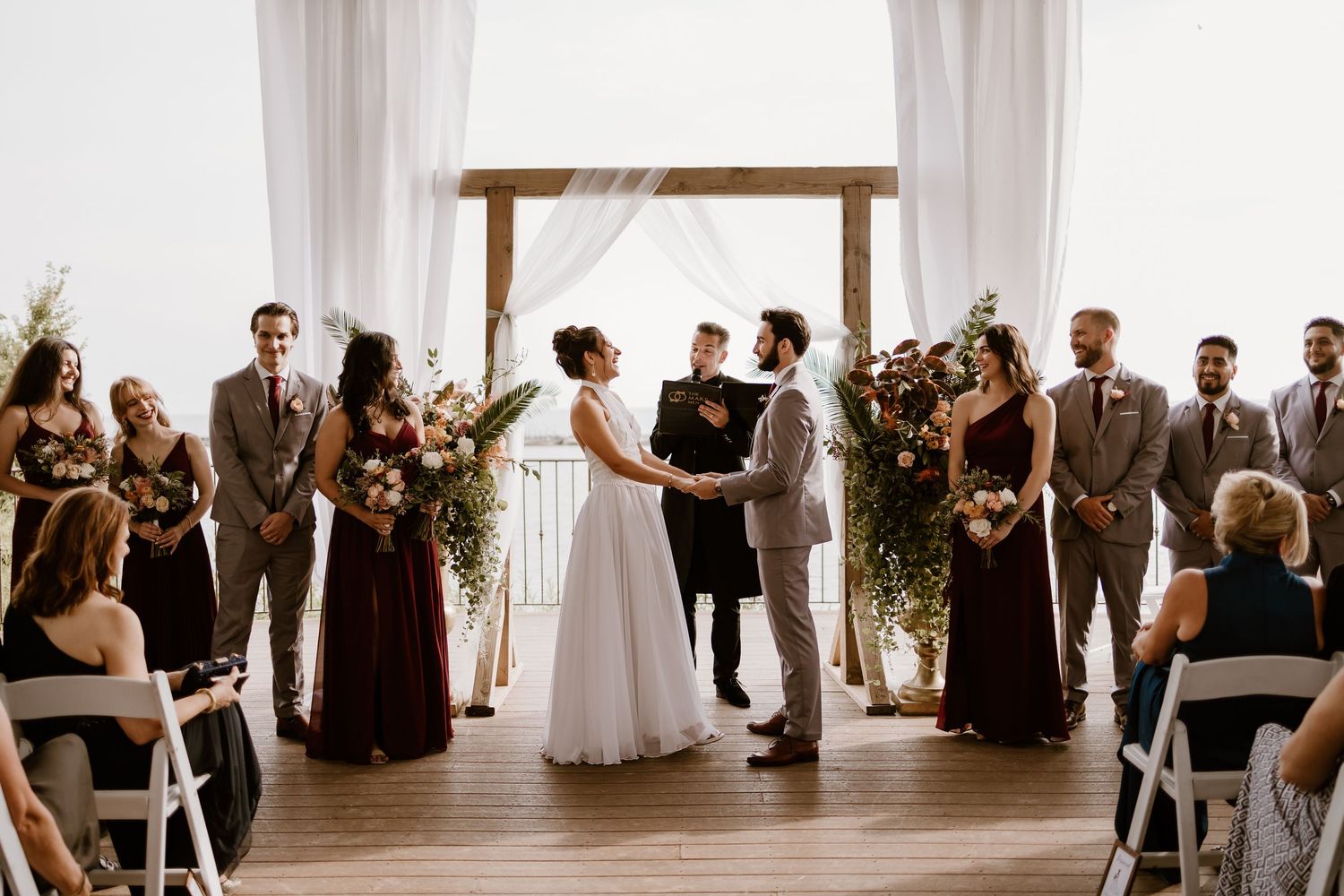Wedding ceremony in progress under white drapes with floral decorations.