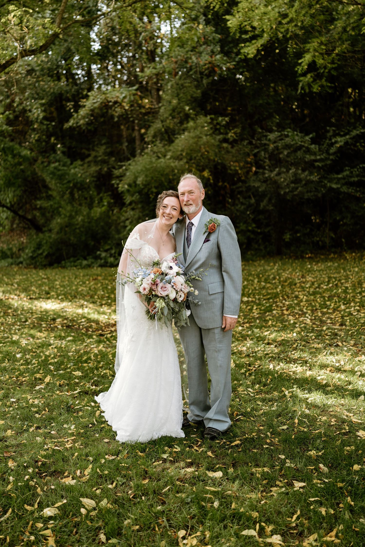 Newlyweds pose for a portrait on grass covered with fallen autumn leaves.