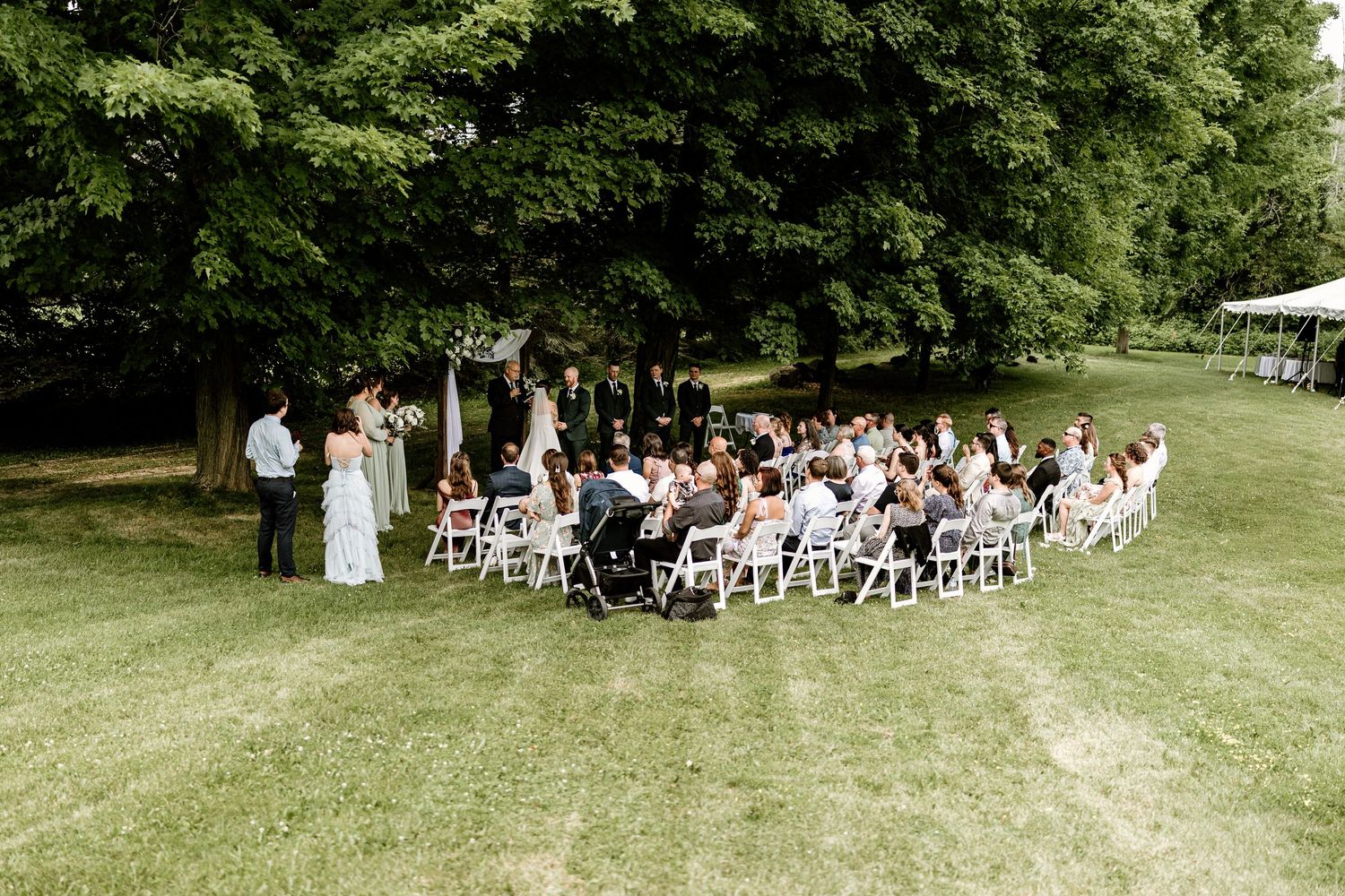 Outdoor wedding ceremony setup with white chairs arranged on a green lawn.