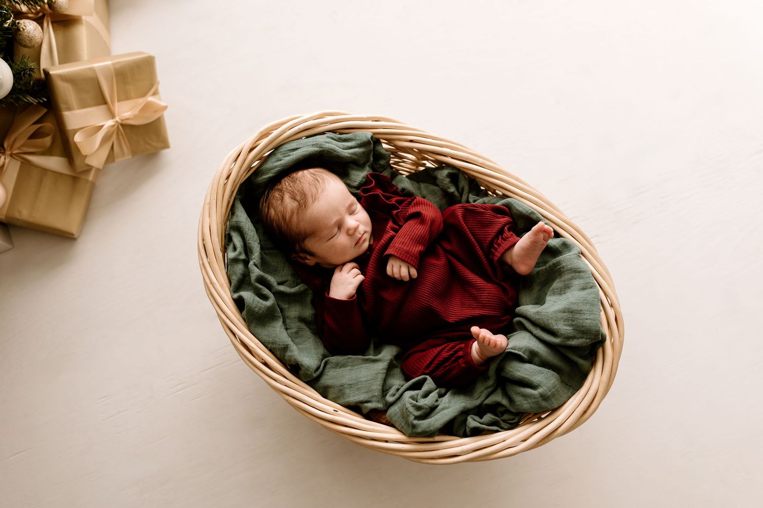 Sleeping newborn baby nestled in woven basket with red and green fabric.