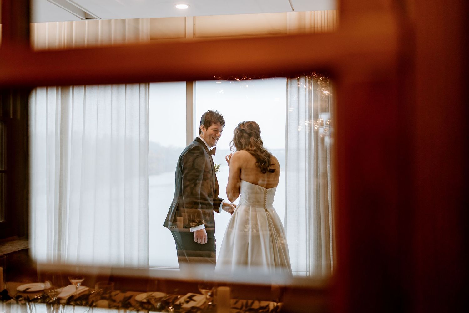 Intimate wedding ceremony moment captured in a room with soft window light and sheer curtains.