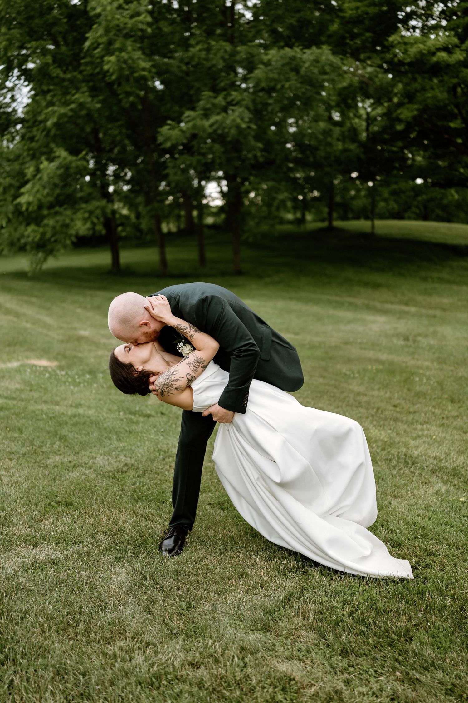 Dramatic dip kiss pose on green lawn during wedding photoshoot.