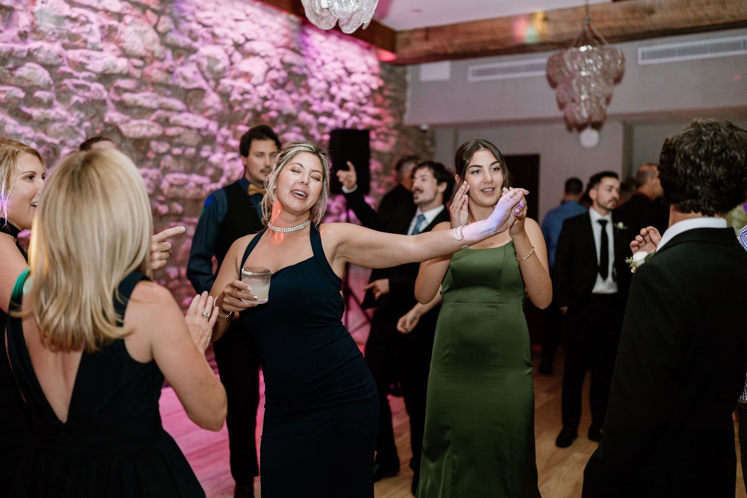Wedding celebration with pink lighting and guests dancing on wooden floor.