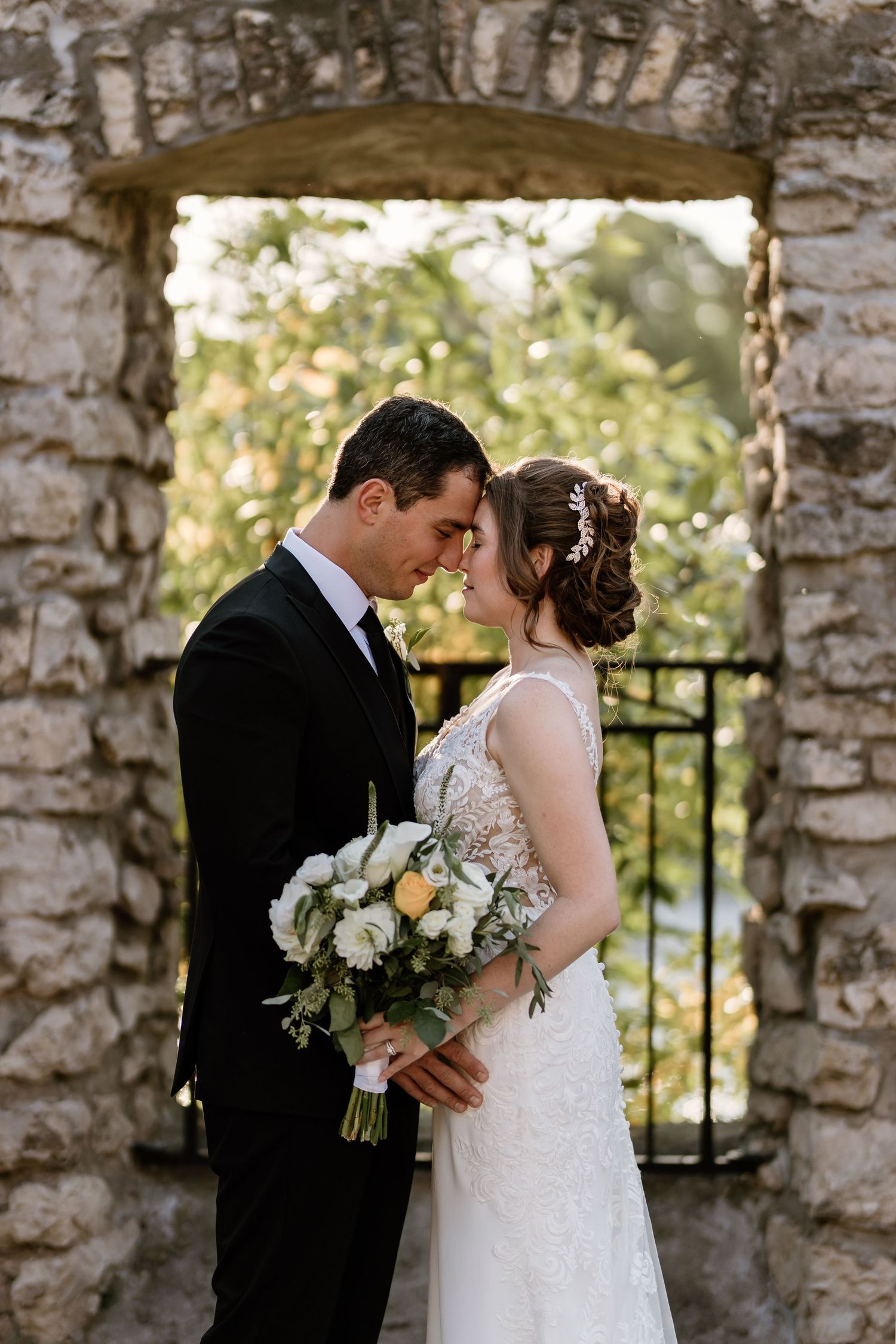 Intimate wedding moment captured against rustic stone wall with natural lighting.