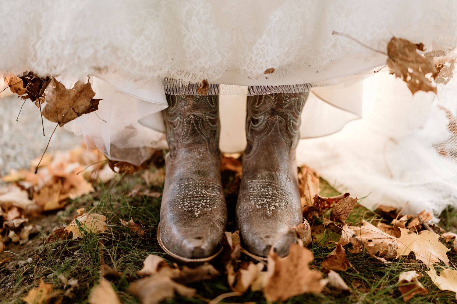 Wedding shoes and dress hem visible among scattered autumn leaves on the ground.