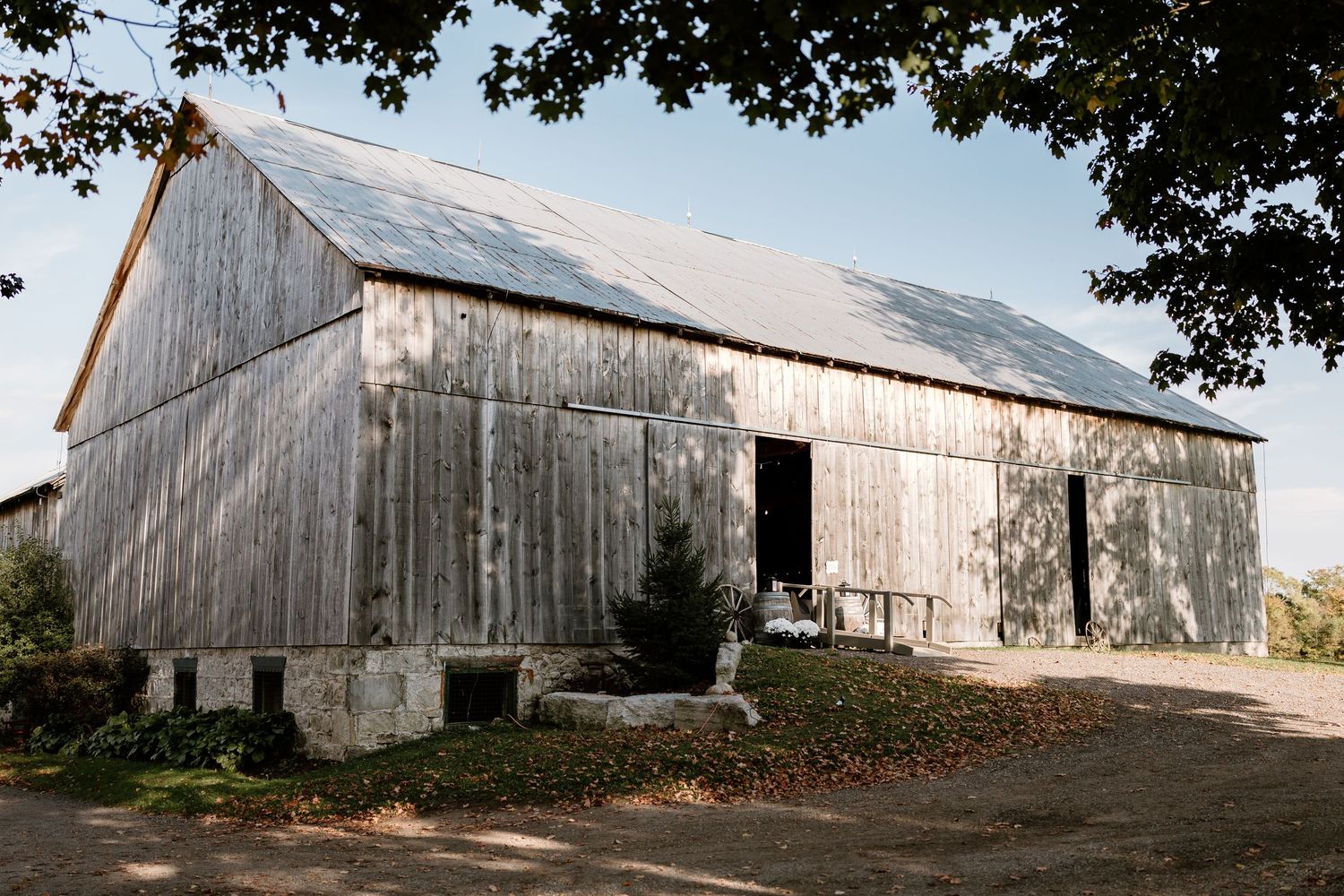 Weathered white barn stretches across rural landscape under blue sky.