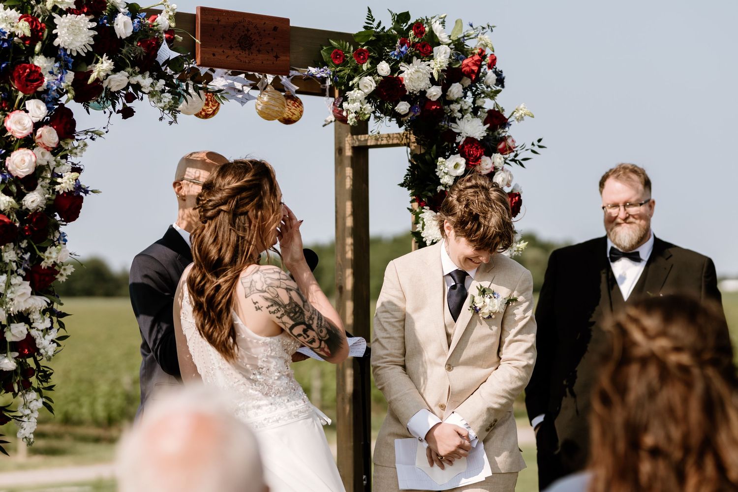 Wedding ceremony moment under an ornate floral arch with roses and greenery.