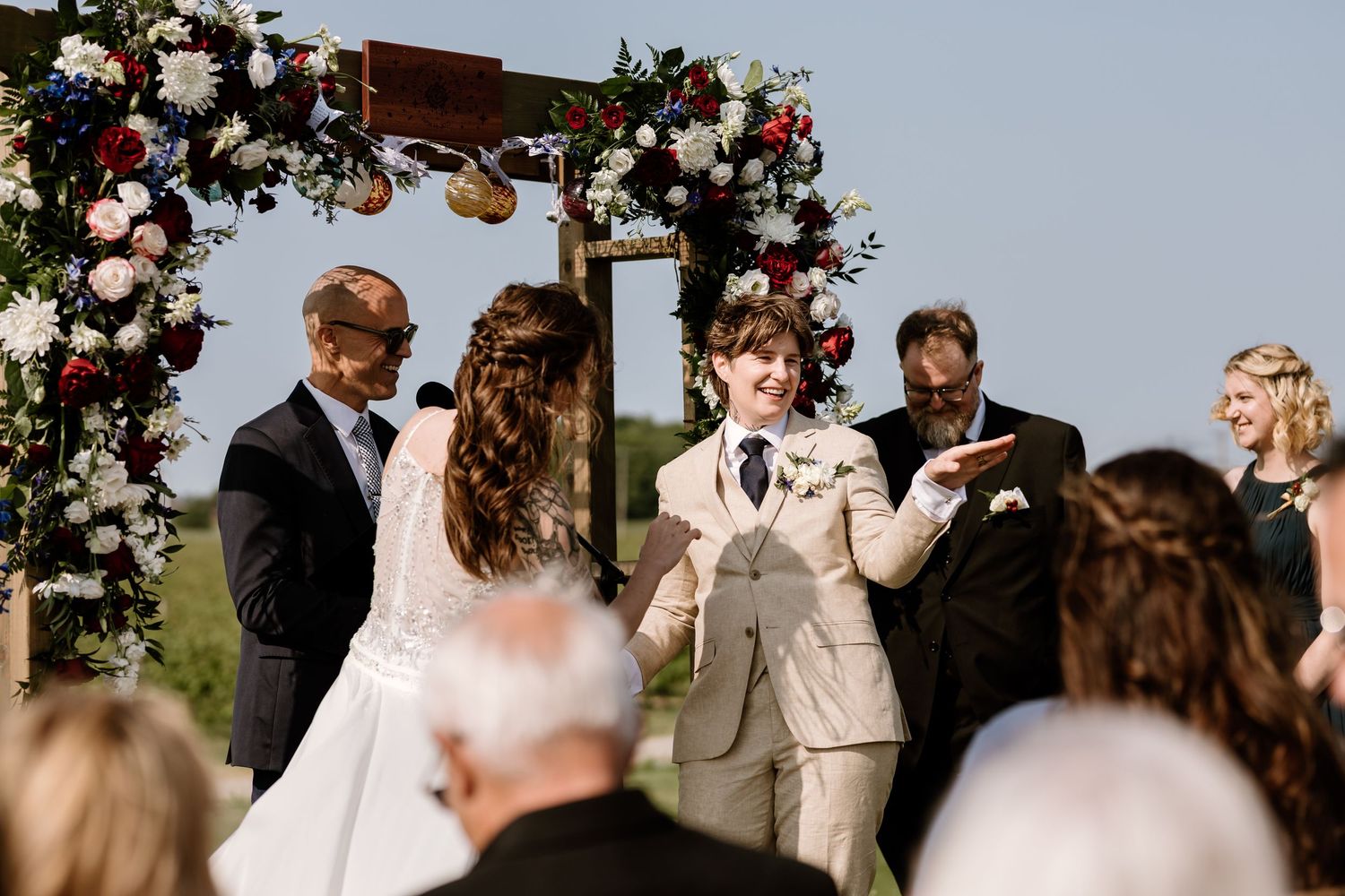 Outdoor wedding ceremony with guests watching under an elegant floral arch decorated with roses.