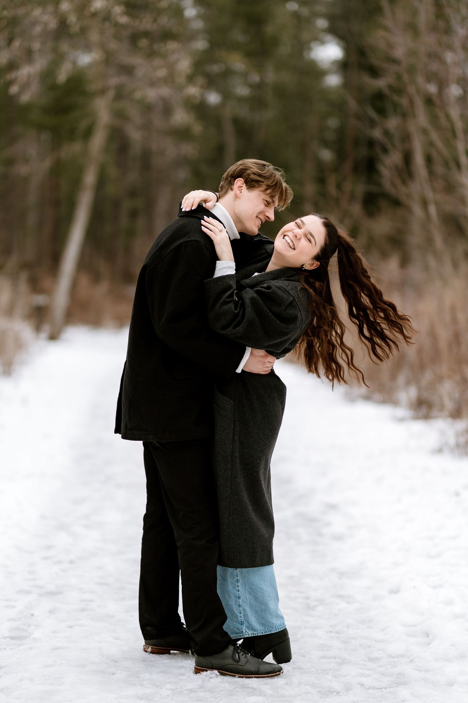 Playful couple dancing and laughing together on snow-covered path.