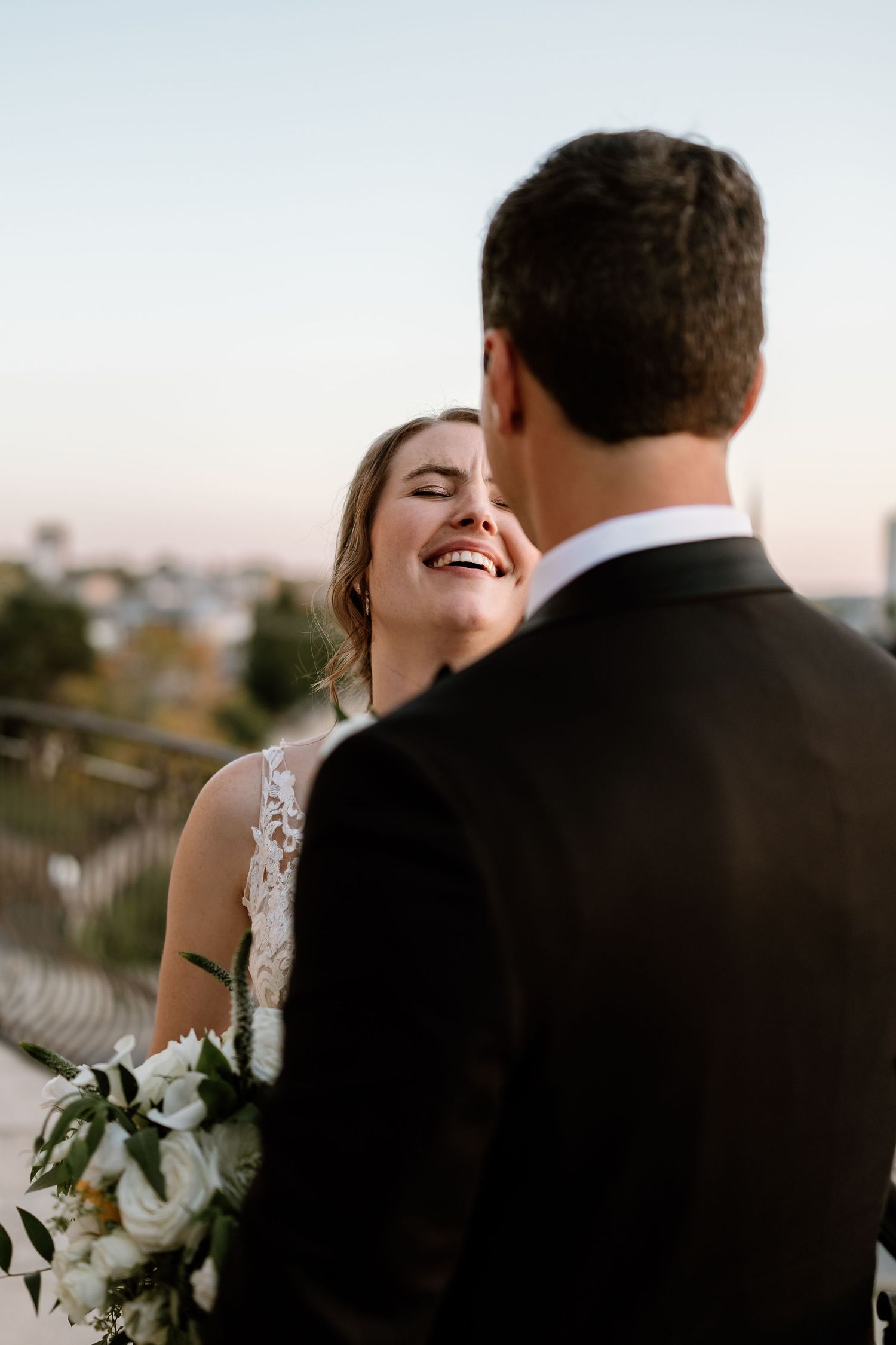 Candid wedding portraits showing joyful laughter against soft sky backdrop.