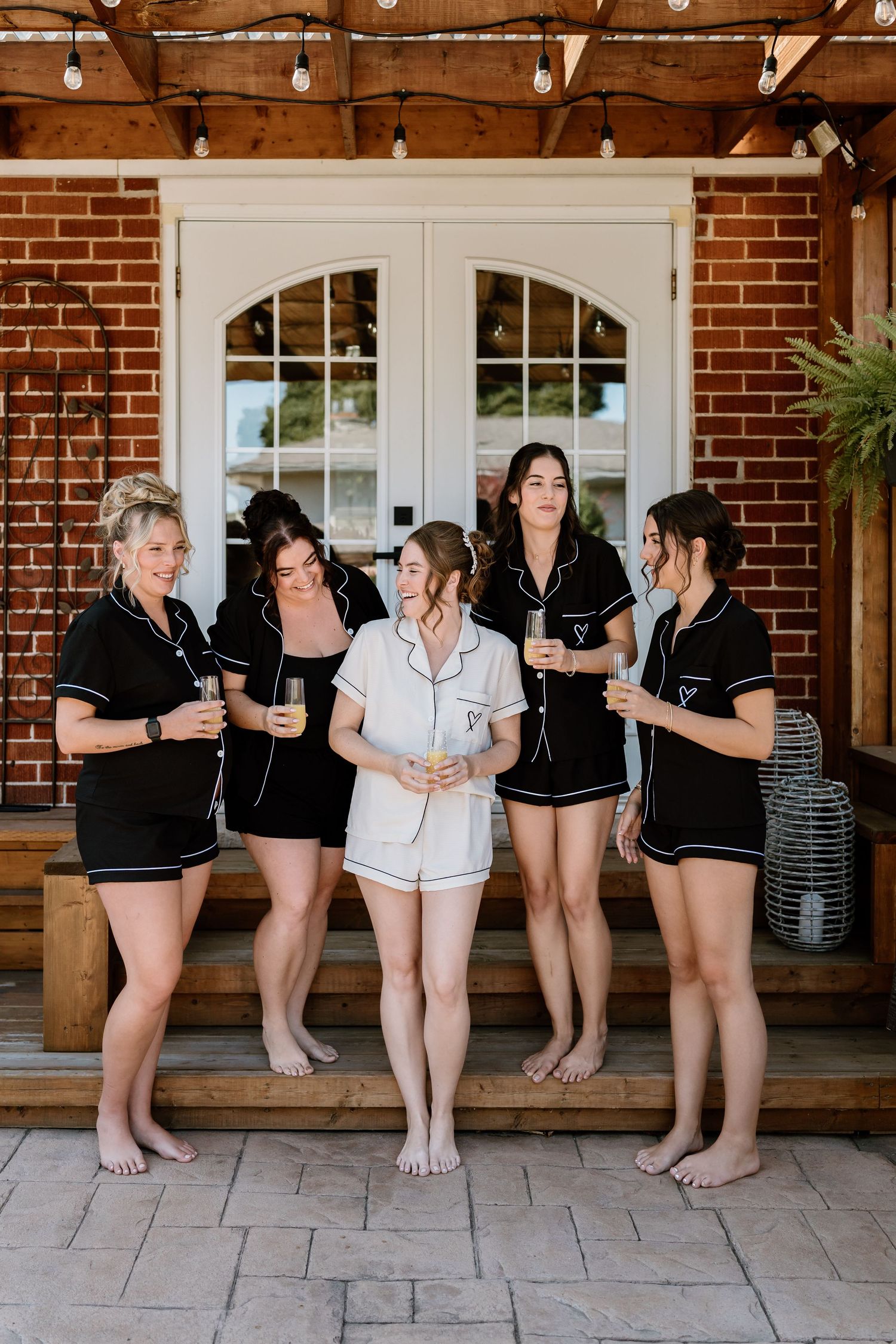 Bridal party in matching robes relaxing on outdoor porch of brick building.
