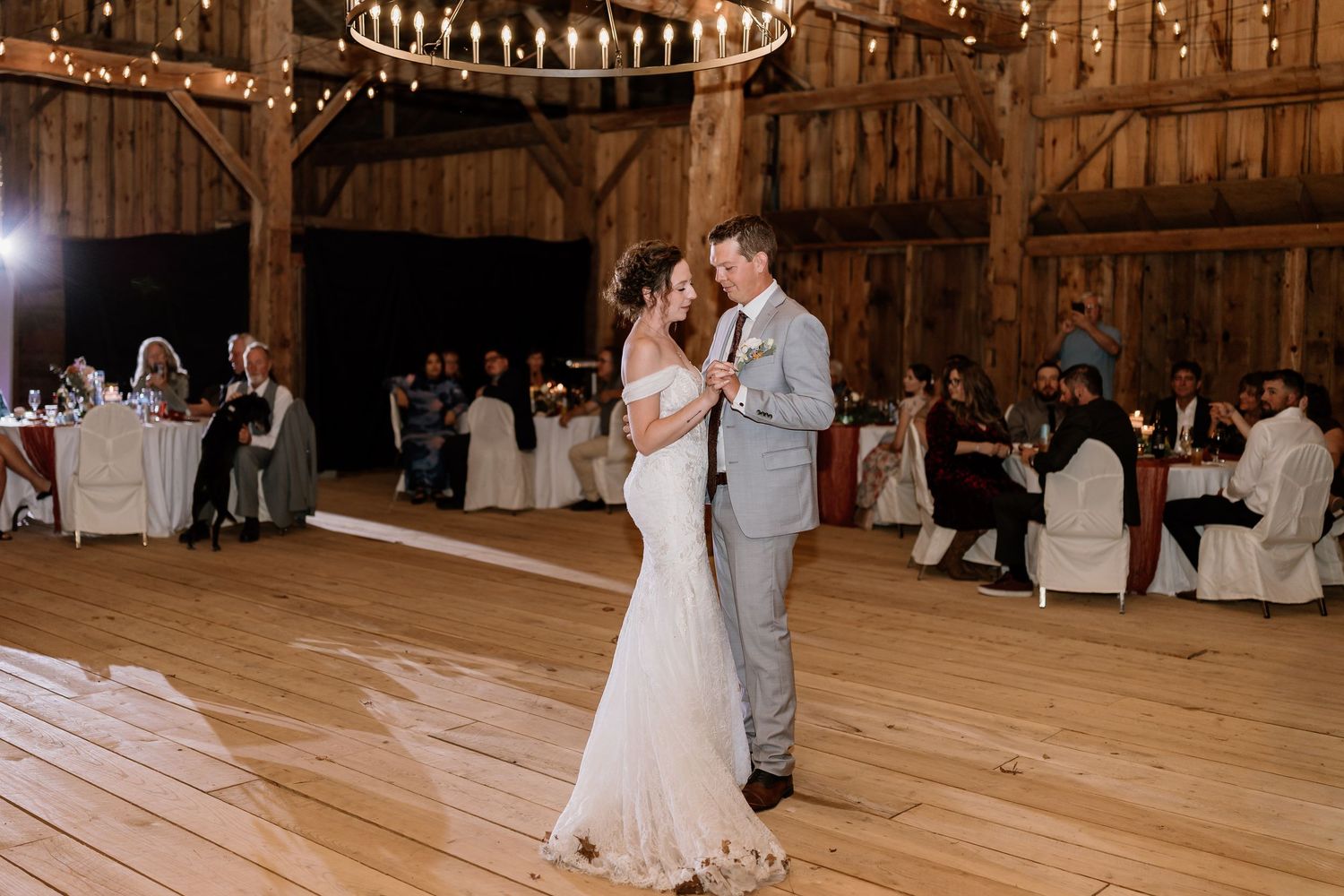 Couples dancing on wooden floor in rustic barn with ambient lighting.