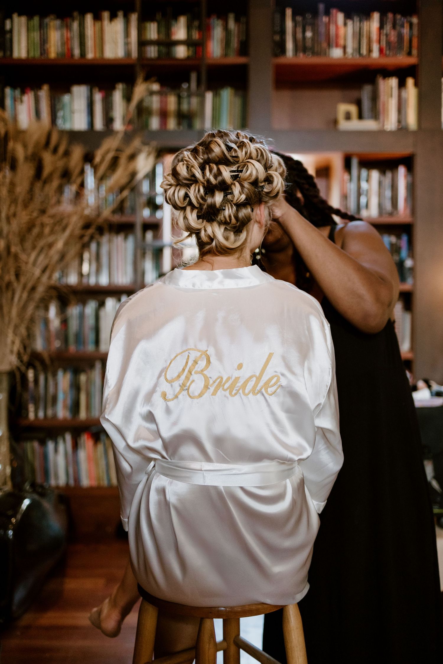 White satin bridal robe with gold lettering photographed in a library setting.