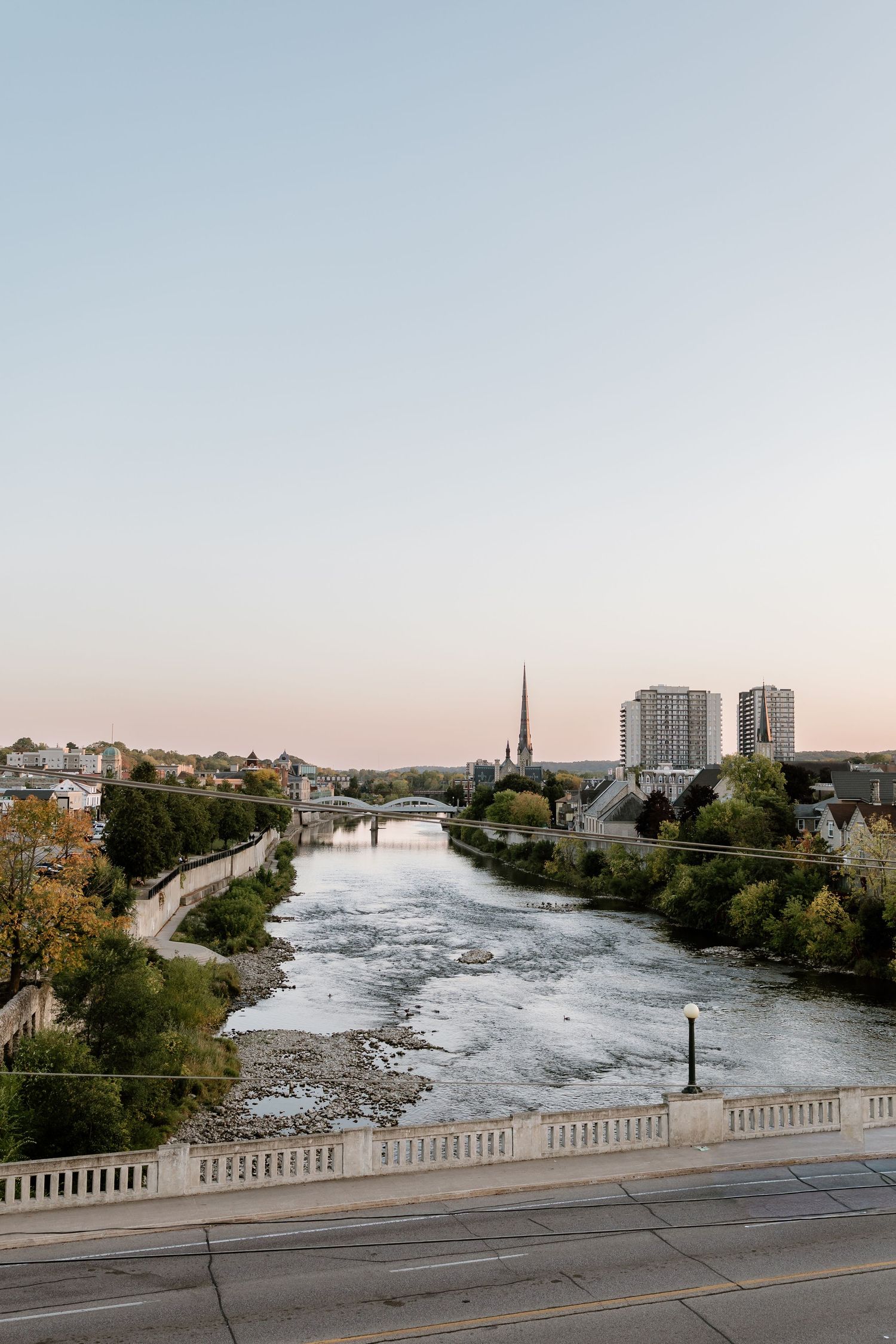 Panoramic view of a river with buildings and trees along its banks during sunset.