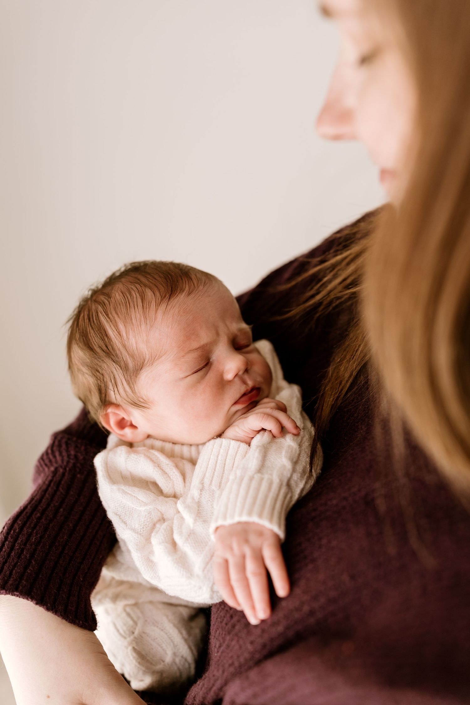 Peaceful newborn in white sweater resting against parent in burgundy sweater.