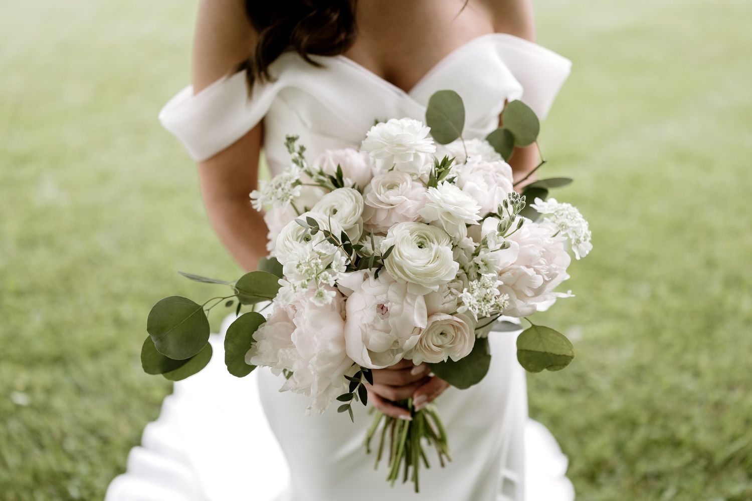 Elegant white bridal bouquet with roses and eucalyptus leaves against a green background.