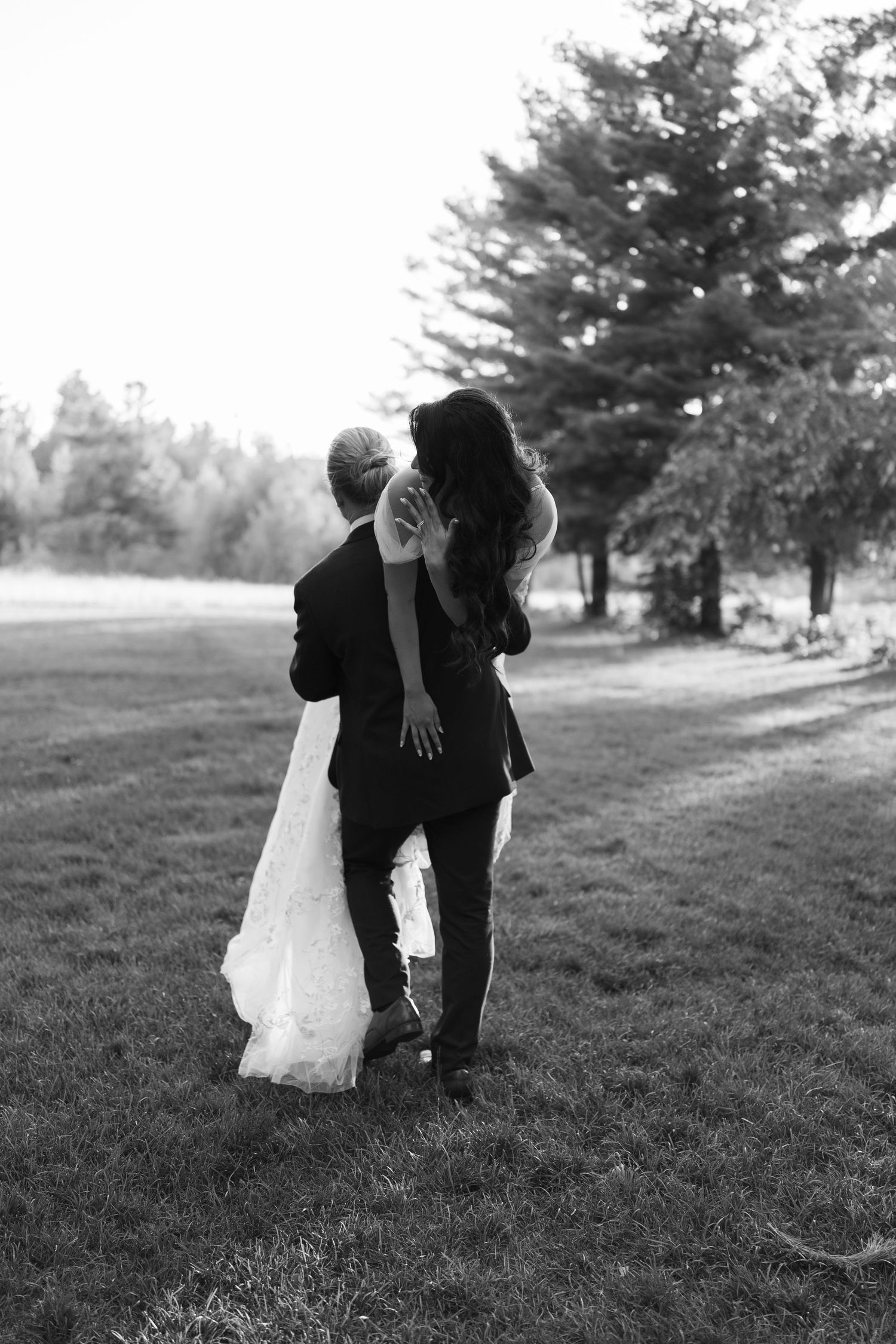 Black and white photo of a couple dancing together on a grassy hillside.