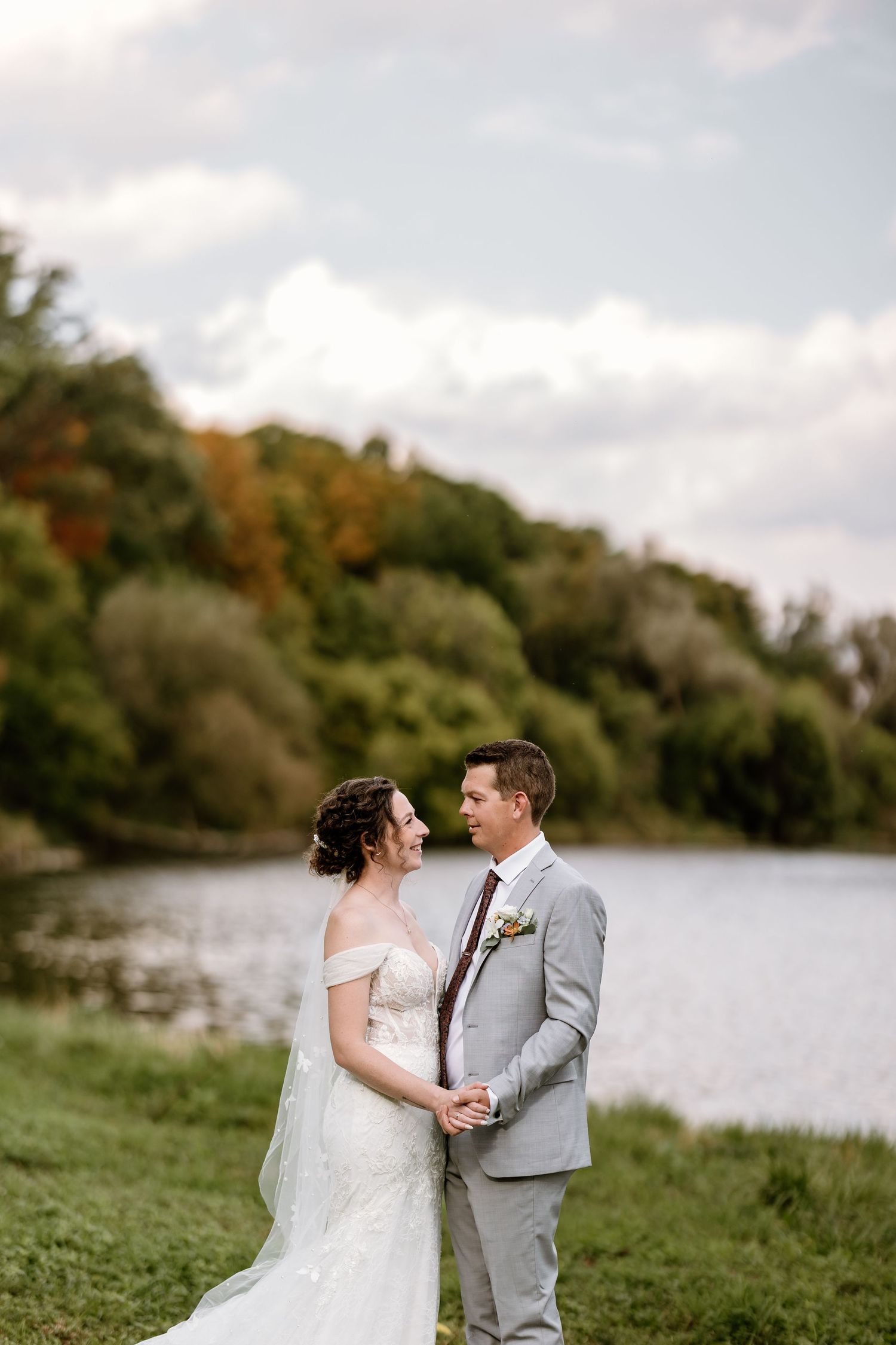 Couple shares intimate moment by lakeside during fall wedding photoshoot.
