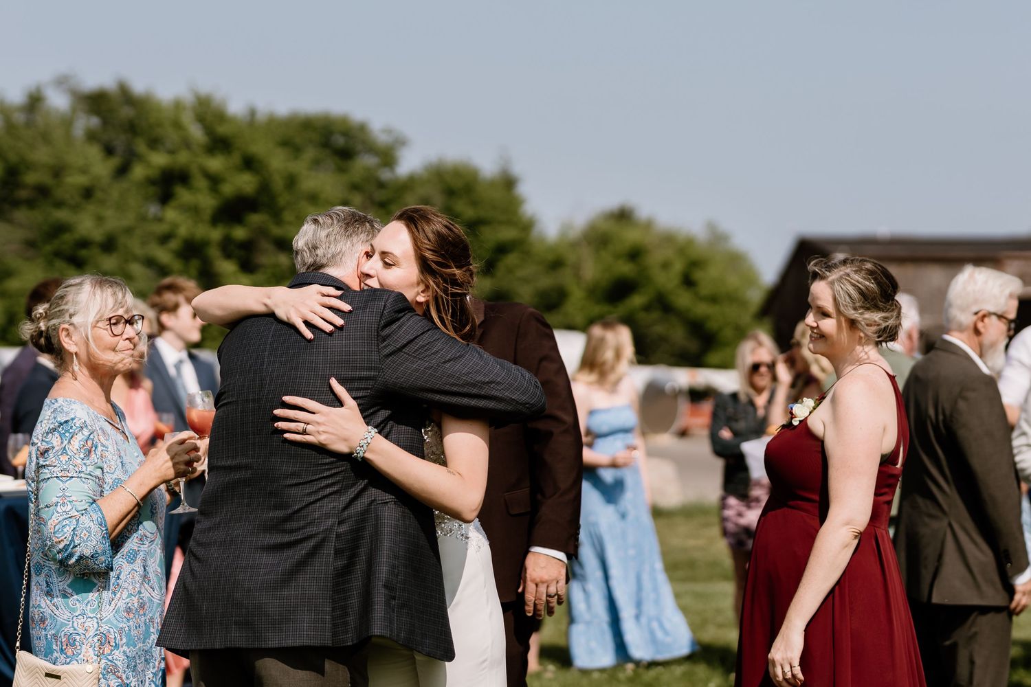 Emotional embrace during outdoor wedding celebration with guests in formal attire.