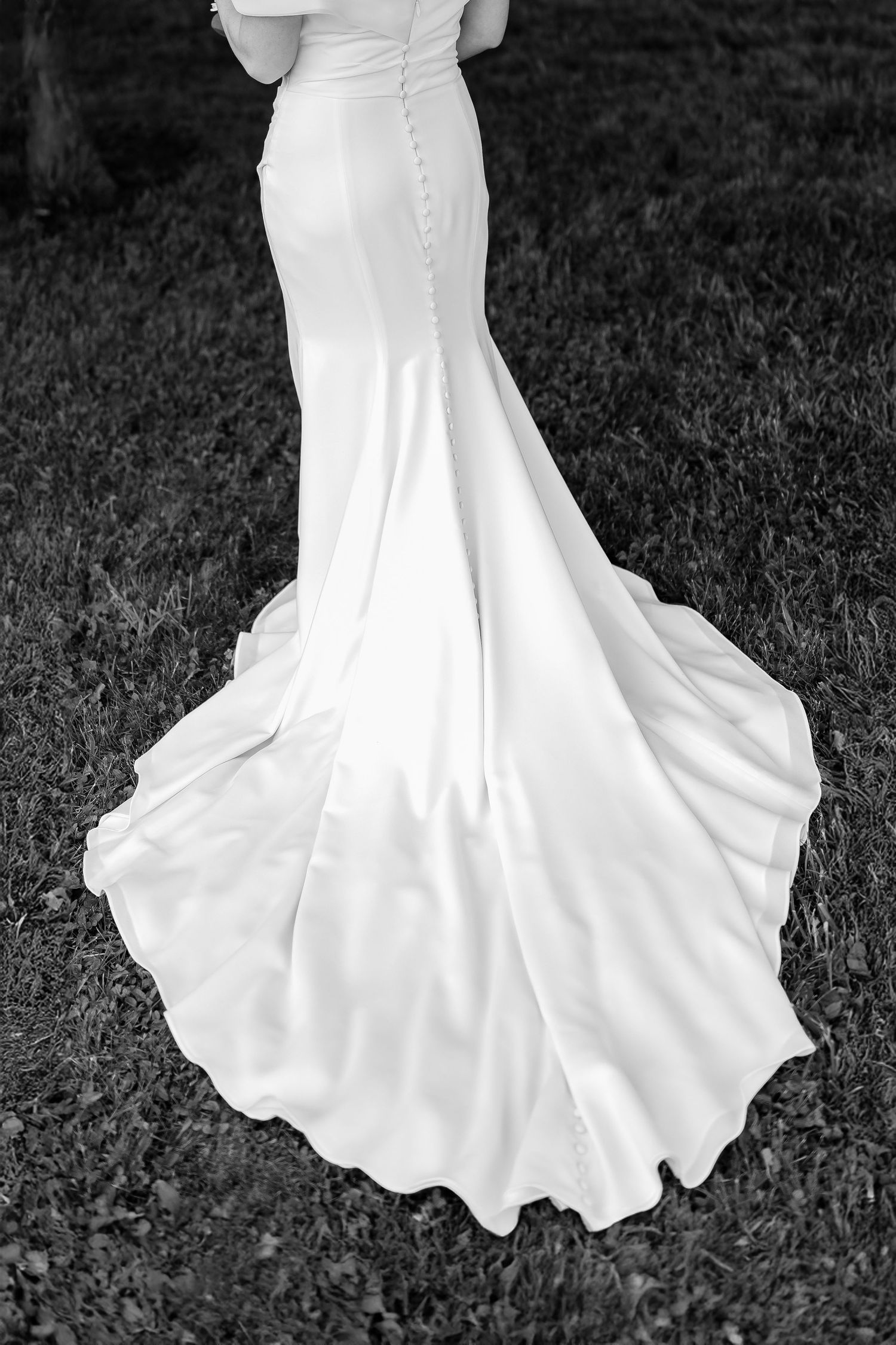 Elegant white wedding dress train spread out on grass in black and white.